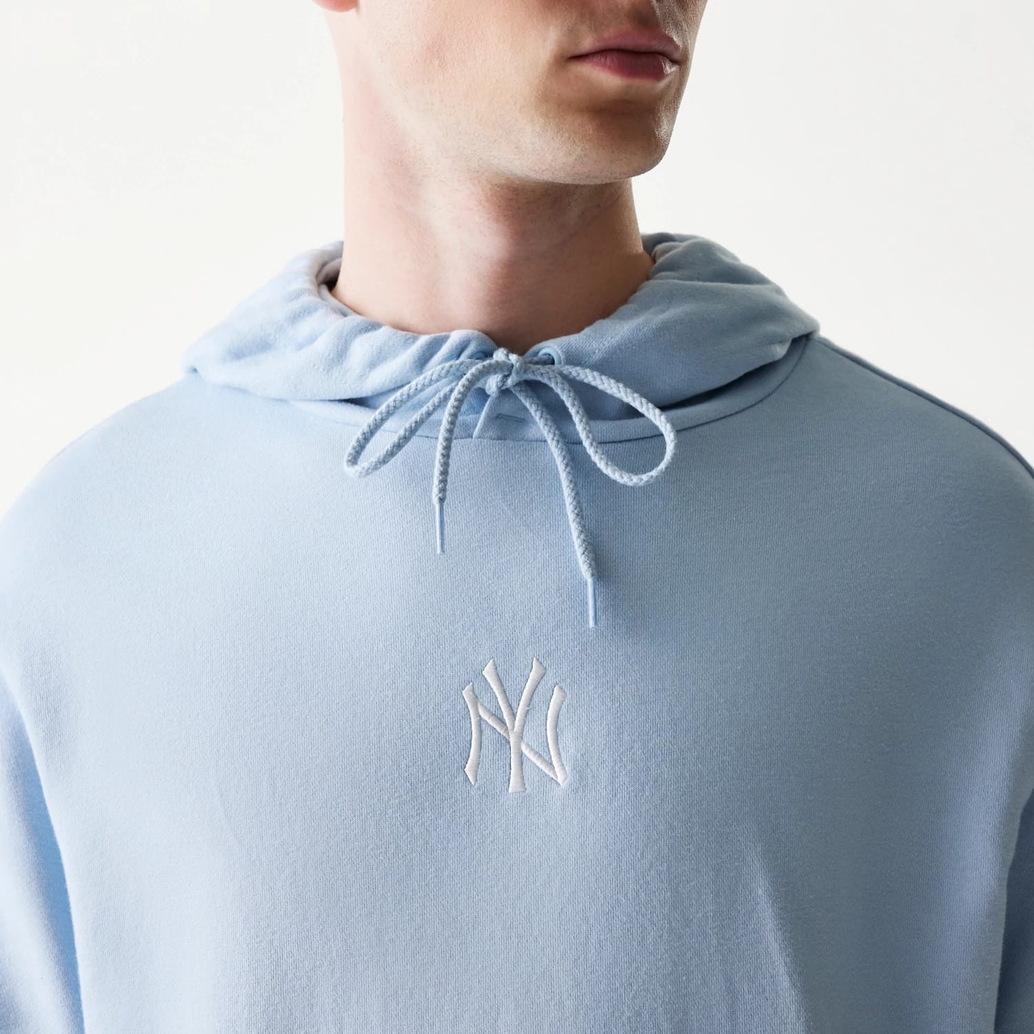 New Era New York Yankees MLB Midi Pastel Blue Oversized Pullover Hoodie, front view on-model showing the light blue hood with drawstrings and a white embroidered Yankees logo centred on the chest.