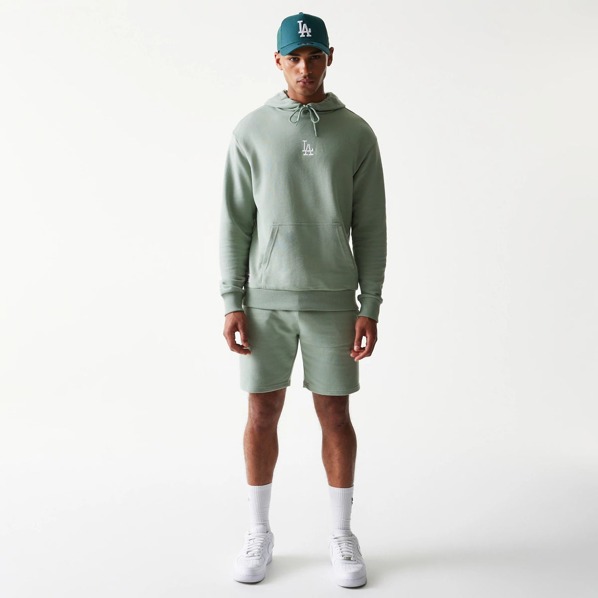 New Era LA Dodgers MLB Midi Green Oversized Pullover Hoodie, front view on a model with matching shorts and cap, displaying an embroidered LA logo on the centre chest and a large kangaroo pocket at the front.