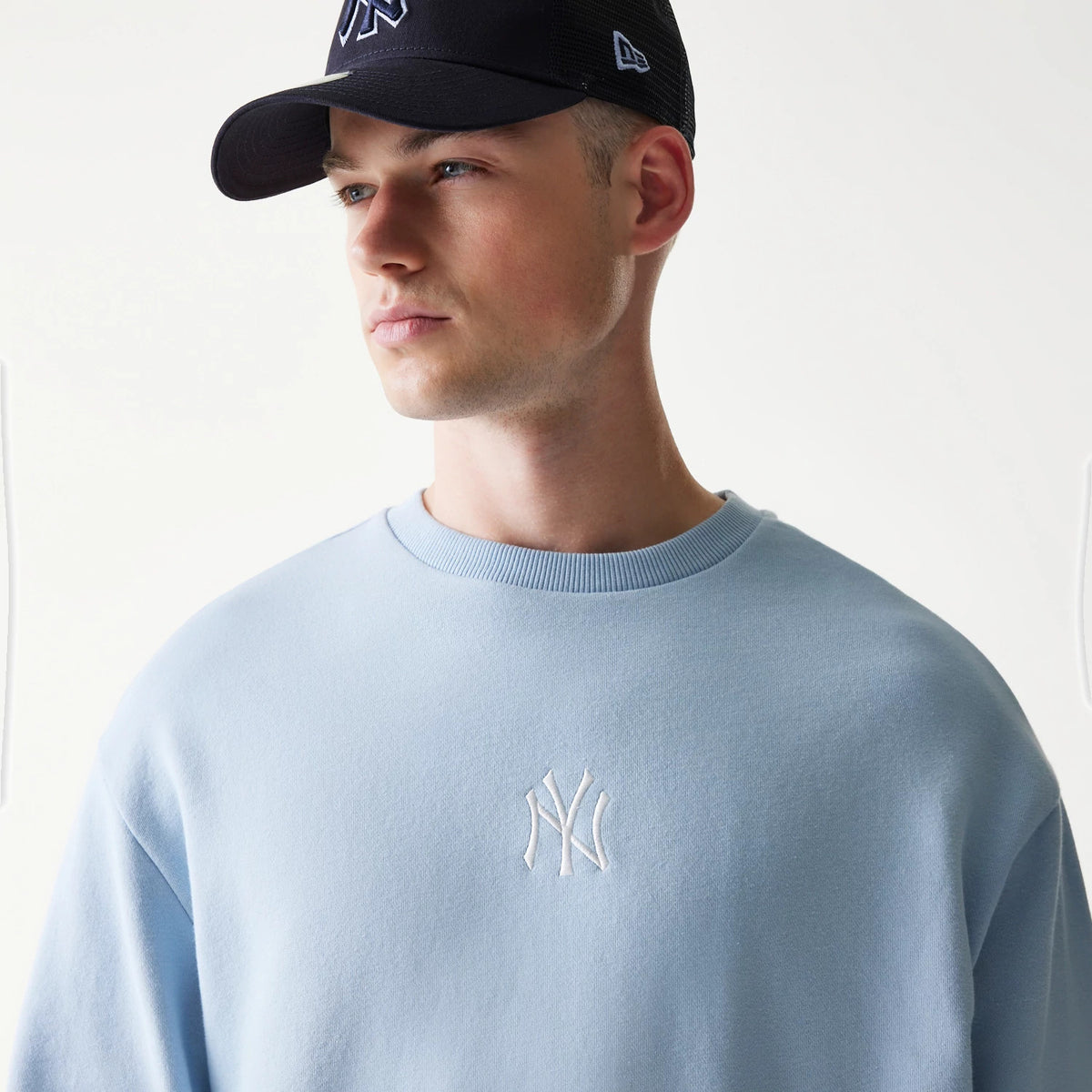 New Era New York Yankees MLB Midi Pastel Blue Oversized Crew Neck Sweater, front view on a model wearing a dark cap, featuring a white embroidered Yankees logo on the chest and ribbed on the crew neck.