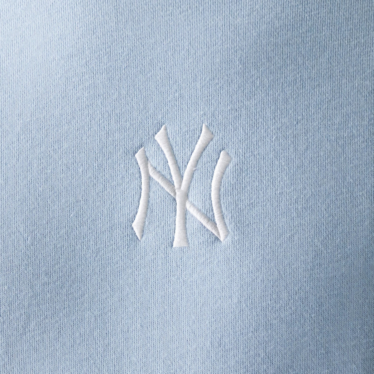 New Era New York Yankees MLB Midi Pastel Blue Oversized Crew Neck Sweater, close-up showing the white textured NY logo embroidered on the pastel blue fabric, highlighting the soft texture and colour of the sweater.