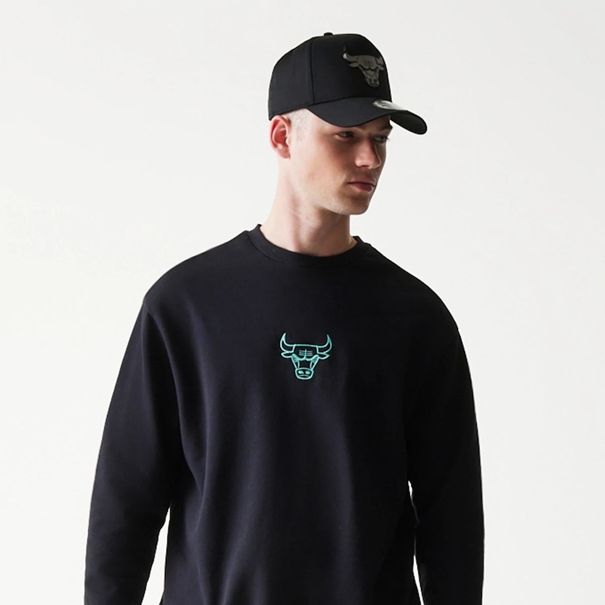 New Era Chicago Bulls NBA Black Oversized Crew Neck Sweater, on-model view with a matching black cap, featuring a teal embroidered Bulls logo on the chest and a relaxed fit crew neck design.