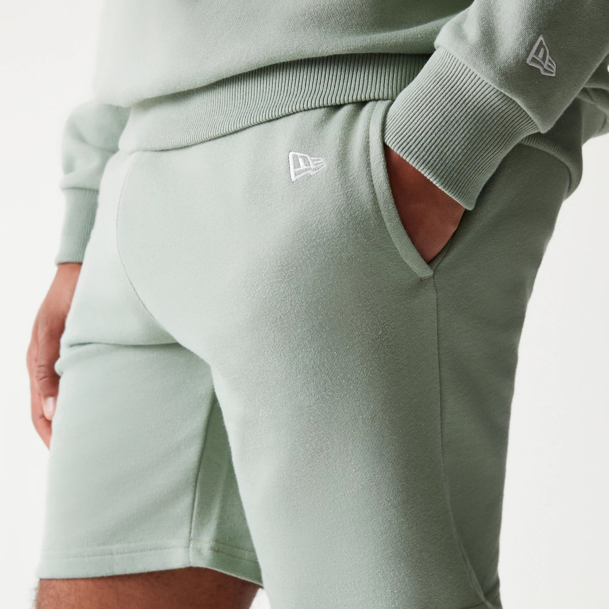 New Era LA Dodgers MLB League Essential Midi Green Shorts, front view on-model showing the pale green shorts with an embroidered New Era logo on the left upper leg, styled with a matching green top featuring the logo on the sleeve.
