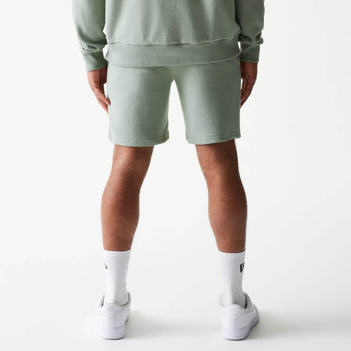 New Era LA Dodgers MLB League Essential Midi Green Shorts, back view on-model showing the soft green fabric reaching just above the knee, paired with matching top and white socks, creating a laid-back, coordinated look.