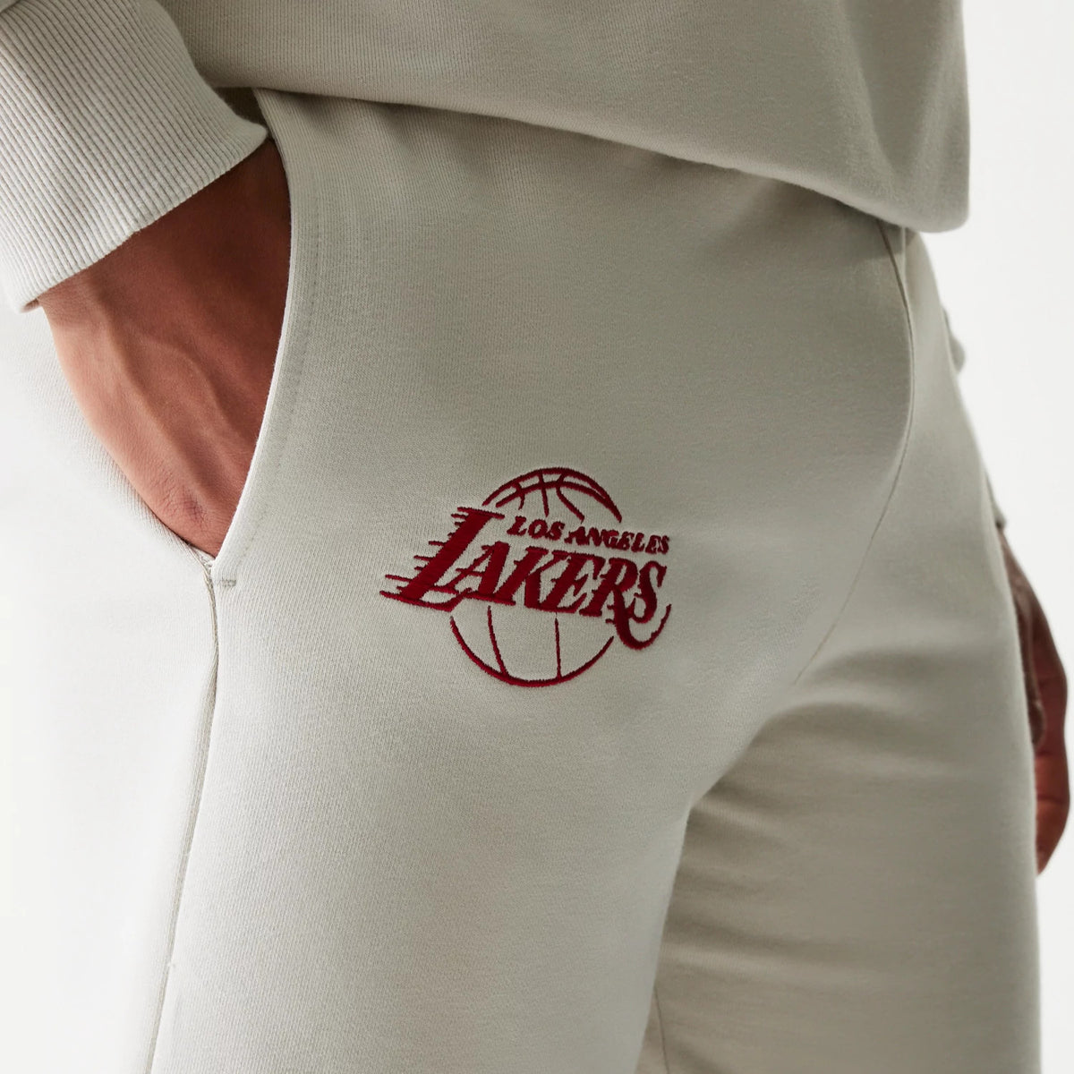 New Era LA Lakers NBA League Essential Light Beige Shorts, side view showing an embroidered red Lakers logo with a basketball graphic on the upper thigh, detailed ribbed waistband and pocket on the hip.
