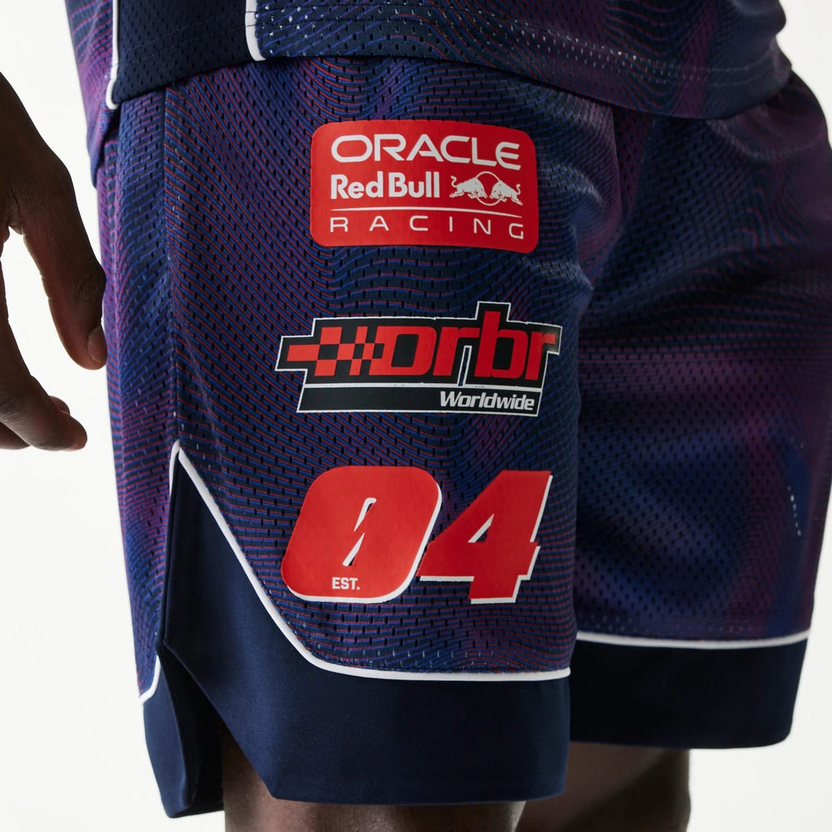 New Era Red Bull Racing Dark Blue Oversized Mesh Shorts, side view showing the dark blue mesh fabric with prominent printed logos including Oracle Red Bull Racing and Drbr Worldwide, along with a large red number 04 near the hem.