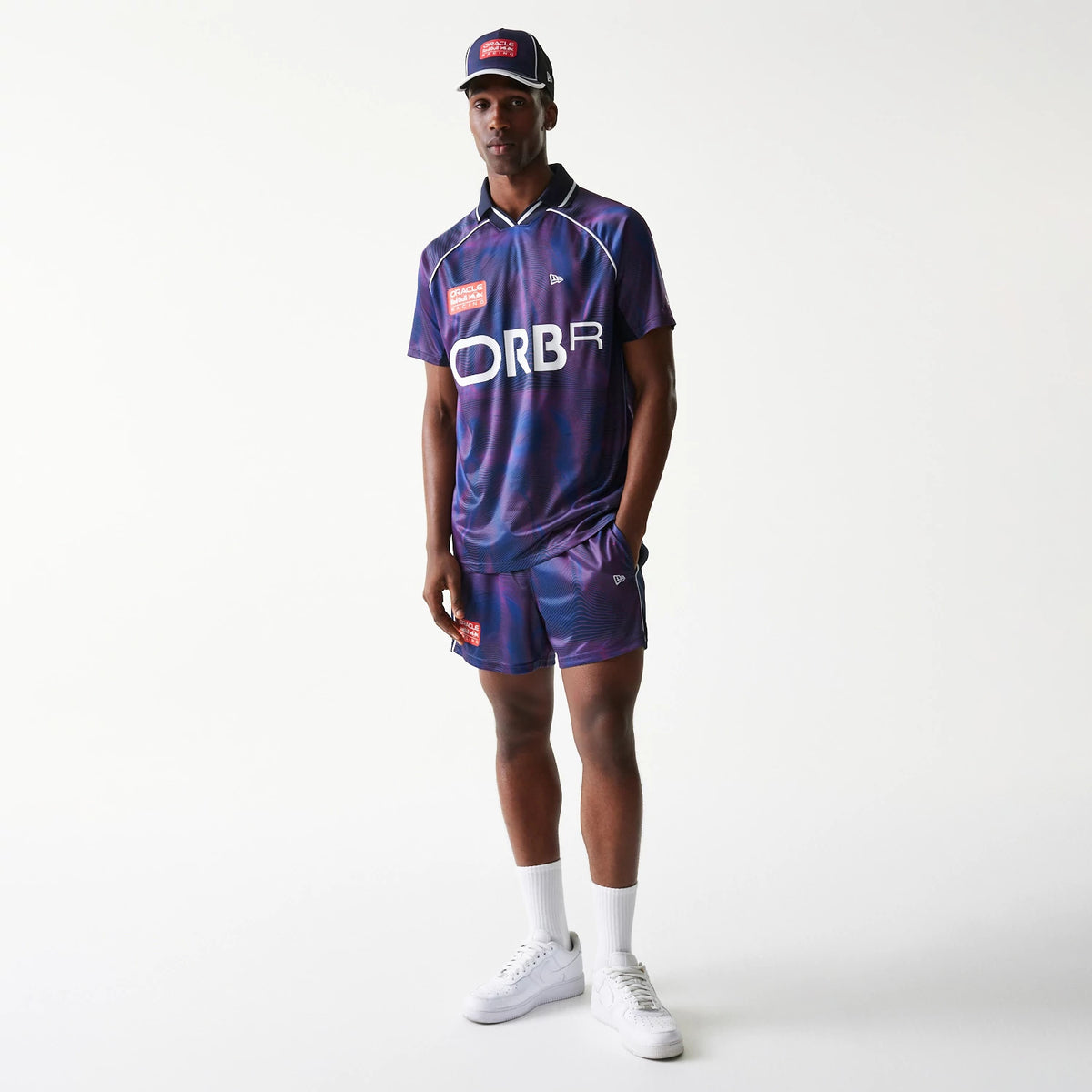 New Era Red Bull Racing All Over Print Dark Blue Football T-Shirt, on-model view showing the print with large ORBR lettering on the front, embroidered New Era logo on the chest, and matching cap and shorts for a coordinated look.