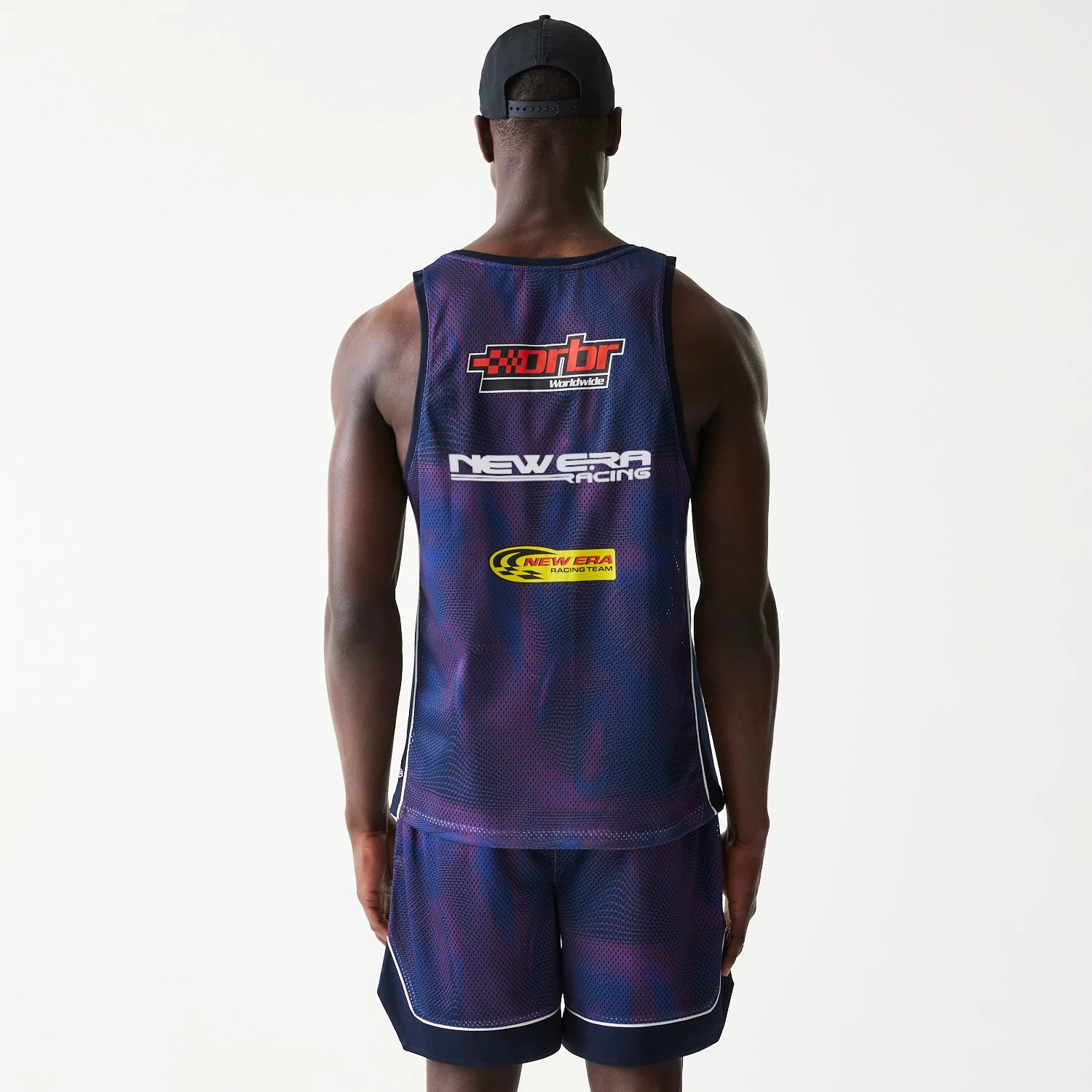 New Era Red Bull Racing Dark Blue Mesh Tank Top, back view on a model wearing matching shorts, showing layered graphics including red rbr lettering, New Era Racing text, and the yellow racing team logo across the back.