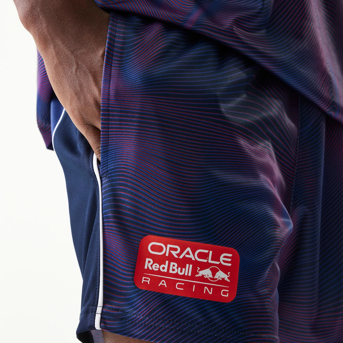 New Era Red Bull Racing All Over Print Dark Blue Football Shorts, side view showing a close-up of the gradient pattern with thin horizontal red and blue lines and a white embroidered Oracle Red Bull Racing logo near the hem.