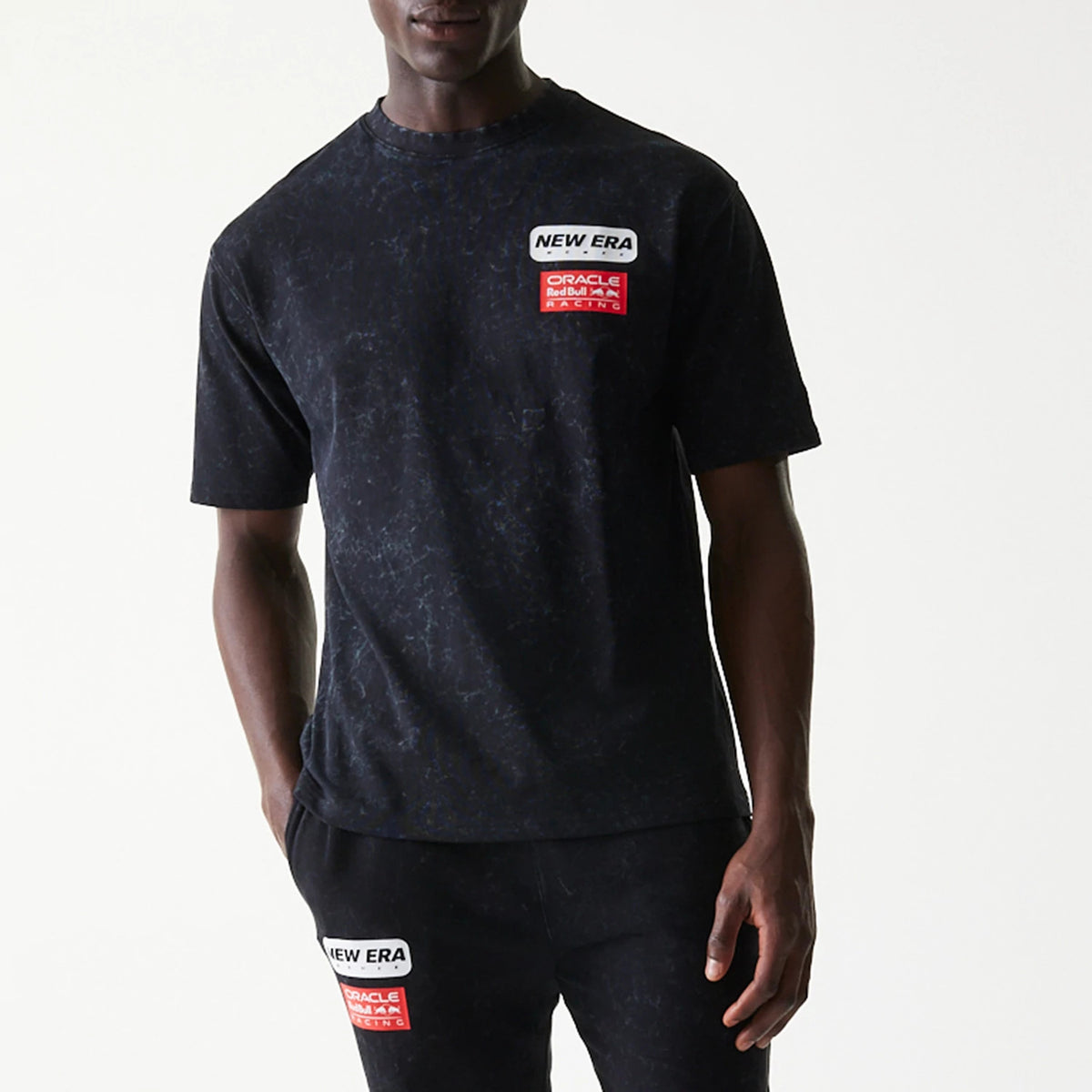 New Era Red Bull Racing Linear Graphic Black Oversized T-Shirt, front view on-model showing a dark marbled pattern and prominent white and red printed patches on the upper chest, with matching design on the shorts.