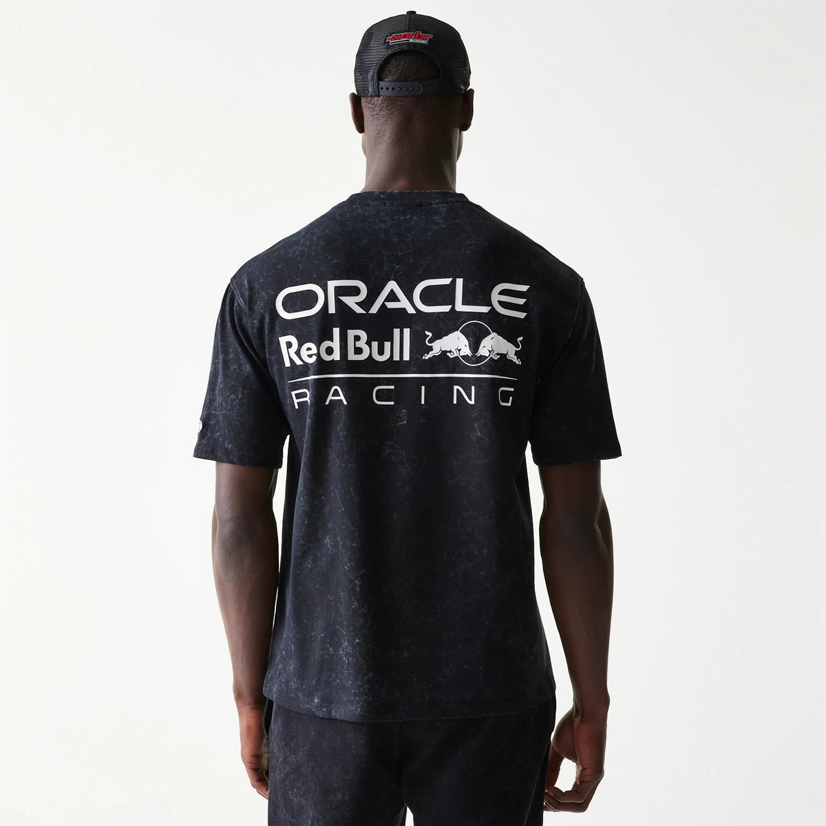 New Era Red Bull Racing Linear Graphic Black Oversized T-Shirt, back view on a model showing large white printed Oracle Red Bull Racing logo across the upper back against a marbled black background.