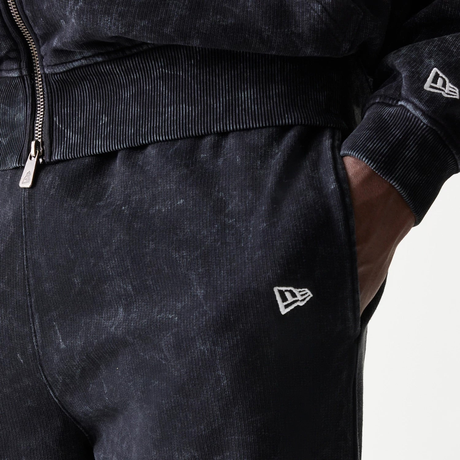 New Era Red Bull Racing Straight Leg Black Straight Leg Joggers, close-up view showing white embroidered New Era flag logo on the left hip, with ribbed waistband and the model's hand in the pocket.