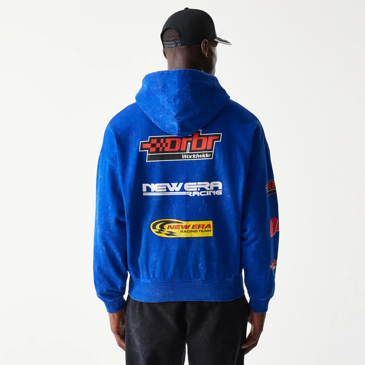 New Era Red Bull Racing Graphic Blue Dropped Shoulder Full Zip Hoodie, back view on-model showing large printed graphics including DRBR Worldwide, New Era Racing, and New Era Racing Team logos across the back of the blue hoodie.