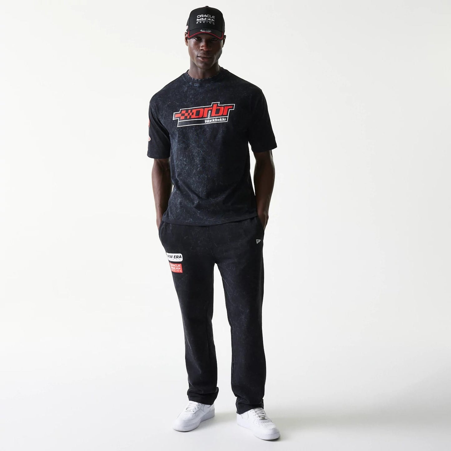 New Era Red Bull Racing Graphic Black Oversized T-Shirt, front view on-model featuring a prominent red and white logo across the chest, with short sleeves and a relaxed fit, styled with dark trousers and a black cap.