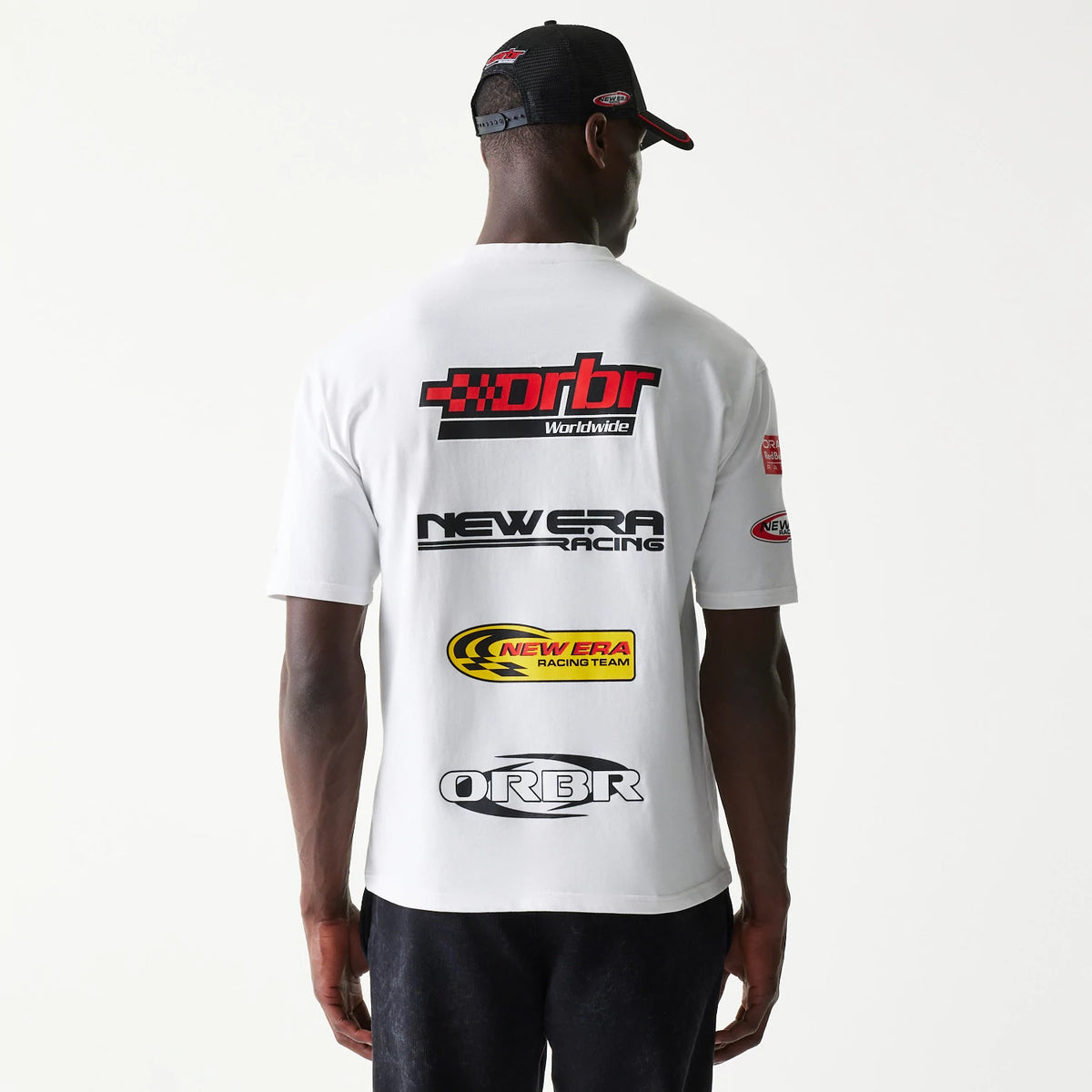 New Era Red Bull Racing Graphic White Oversized T-Shirt, back view on a model showing multiple logos in red, black, and yellow across the back, with New Era branding on the sleeve and a matching cap.