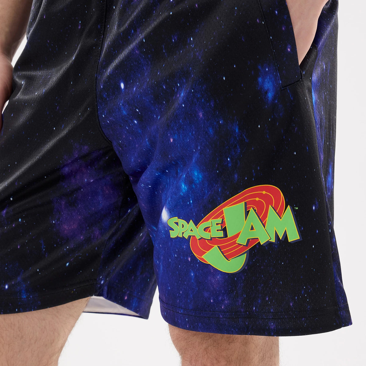 New Era Space Jam Warner Brothers Space Jam White Oversized Shorts, front view showing a galaxy print with a large Space Jam logo in green and red near the hem, styled casually on a model.