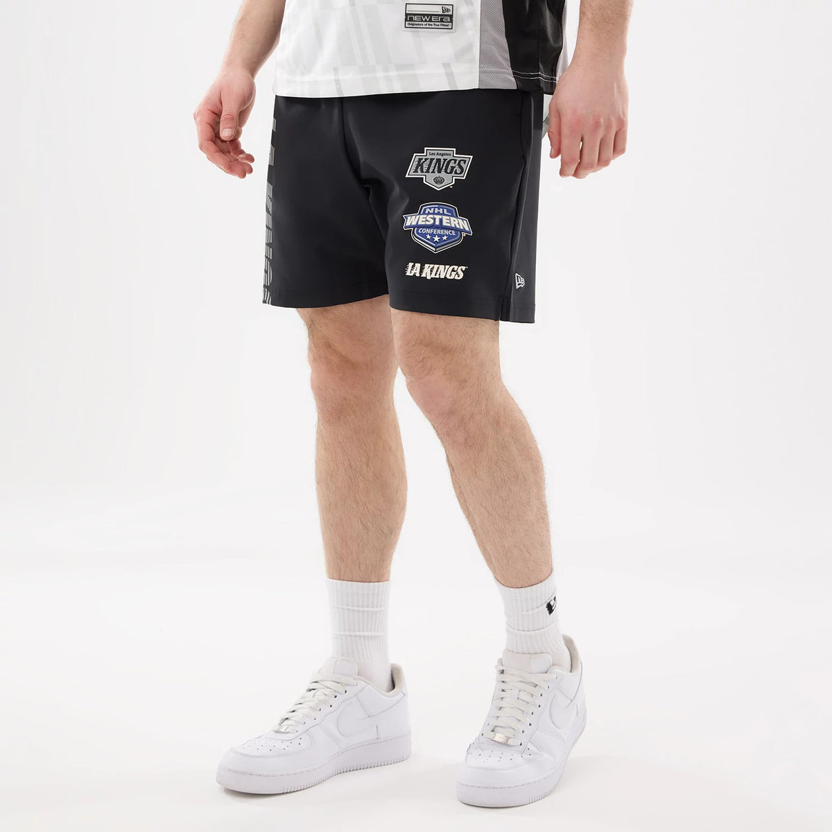 New Era LA Kings NHL Match Black Oversized Shorts, front view on a model showing the large embroidered LA Kings, Western Conference, and team logo patches on one leg, with a small raised New Era logo near the hem.