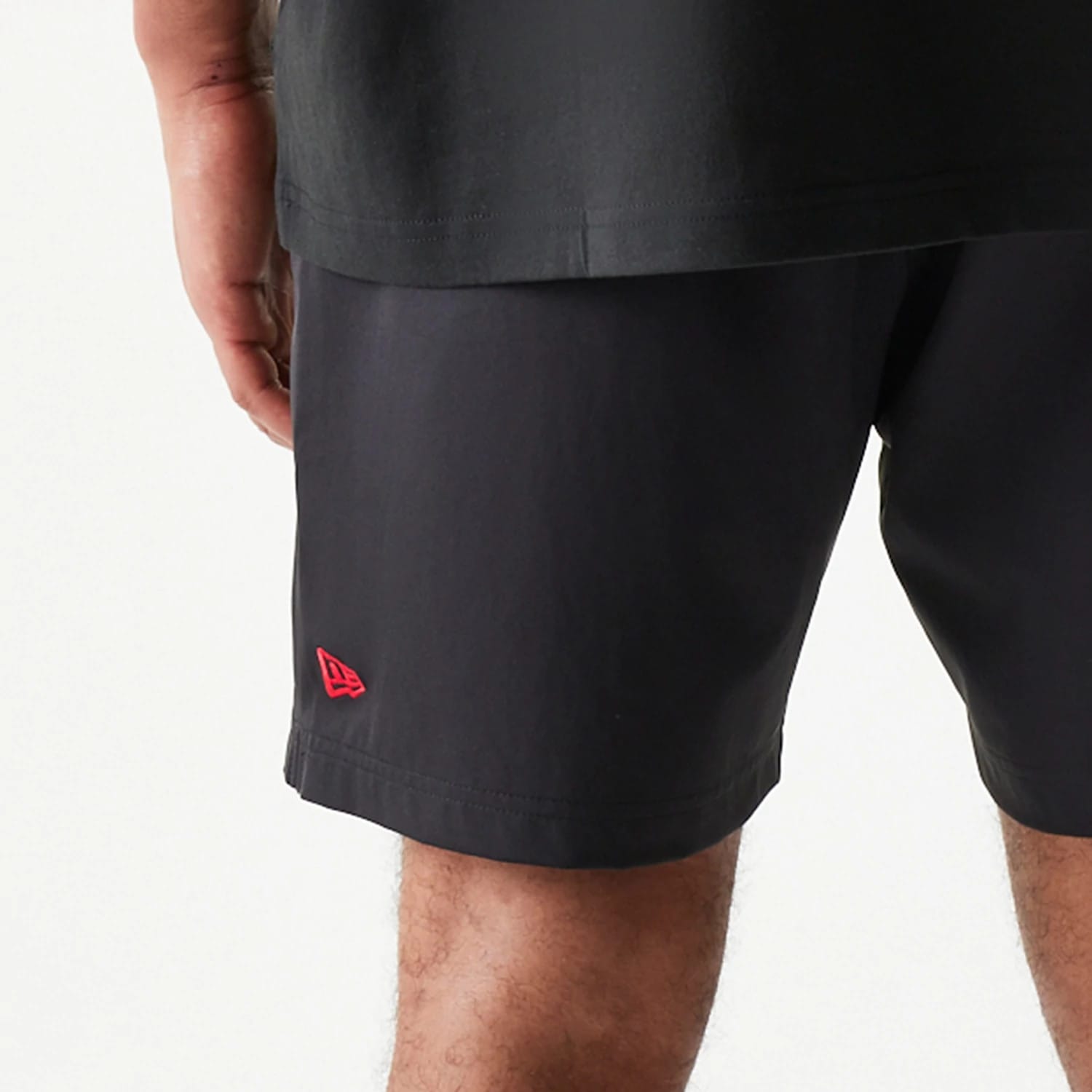 New Era Chicago Bulls NBA Match Black Oversized Shorts, side view showing a red embroidered New Era logo near the hem, worn by a model with a black T-shirt, highlighting the relaxed fit and black fabric.