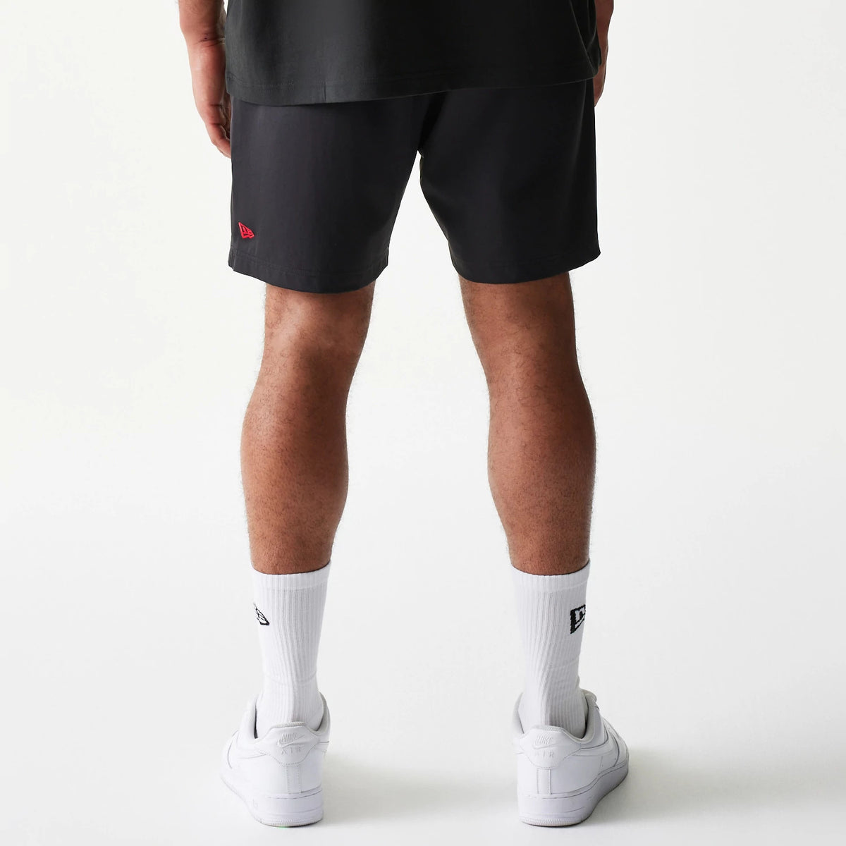 New Era Chicago Bulls NBA Match Black Oversized Shorts, back view on-model showing plain black design with a red embroidered New Era logo on the lower left leg, paired with white socks and trainers.