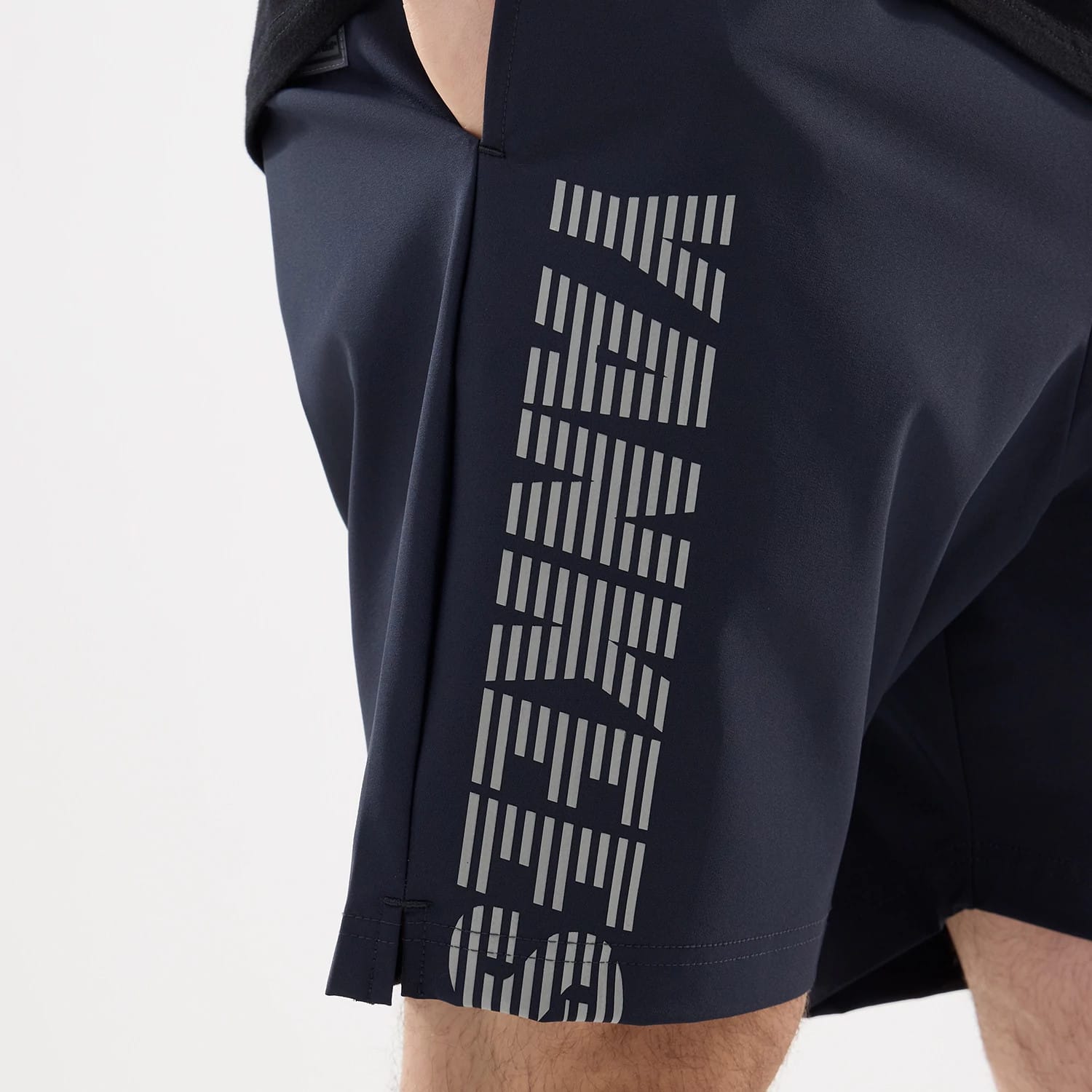 New Era New York Yankees MLB Match Navy Oversized Shorts, side view showing vertical Yankees lettering in reflective silver along the seam, with dark navy fabric and a slanted hem above the knee.