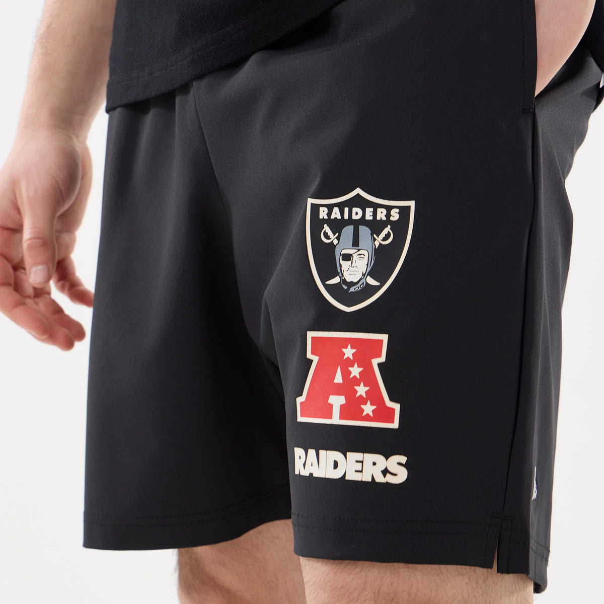 New Era Las Vegas Raiders NFL Match Black Oversized Shorts, three-quarter view showing printed team logos on the left leg, including the Raiders shield and AFC emblem, above a Raiders wordmark.