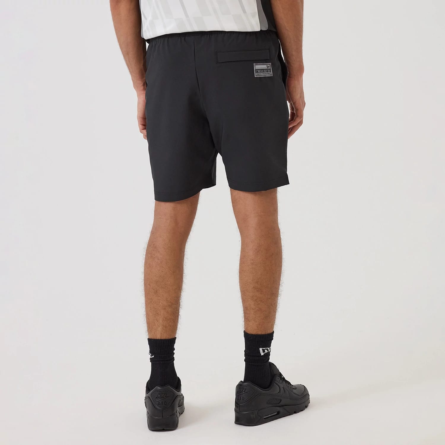 New Era Brooklyn Nets NBA Match Black Oversized Shorts, back view on-model showcasing the simple black design with an elasticated waistband, a rectangular patch with raised lettering on the upper right, and a pocket beneath it.