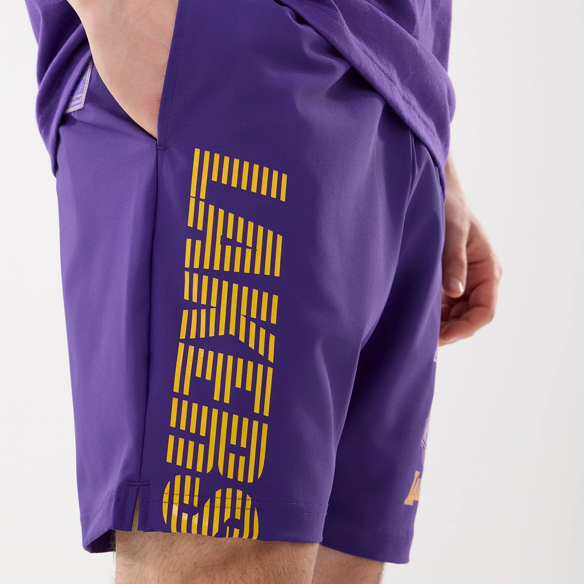 New Era LA Lakers NBA Match Purple Oversized Shorts, side view showing large yellow Lakers lettering running vertically down the right leg against the purple material, worn by a model.