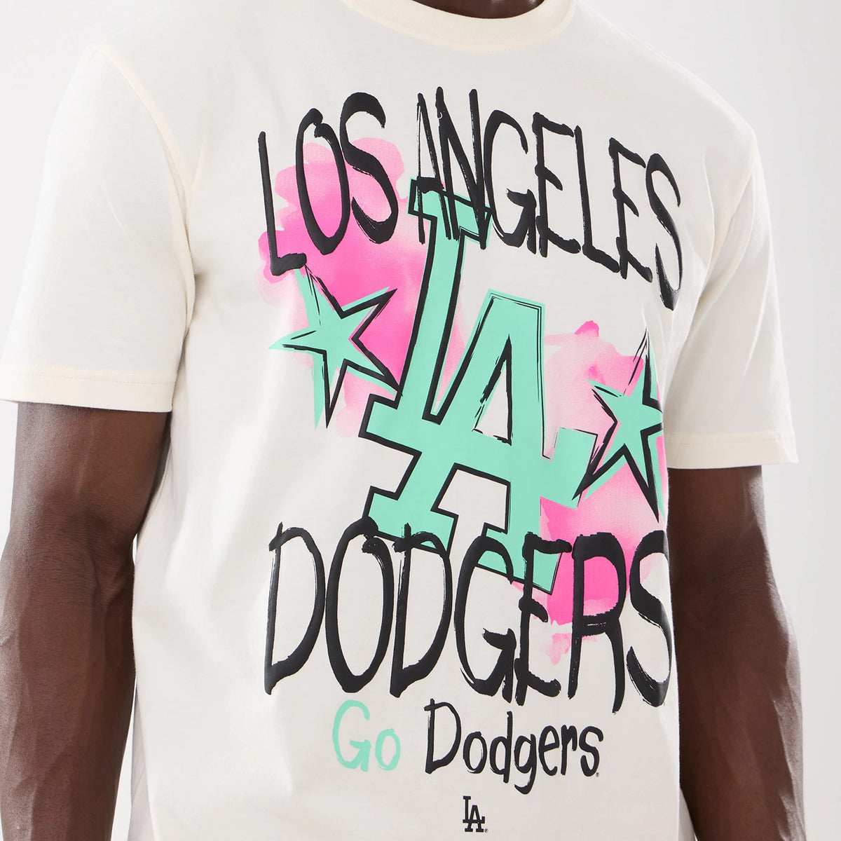 New Era LA Dodgers MLB Street Art Graphic Light Beige T-Shirt, front view showing black and mint green graffiti-style Dodgers text with star motifs and pink splashes, and a small LA logo near the hem on a plain light beige background.