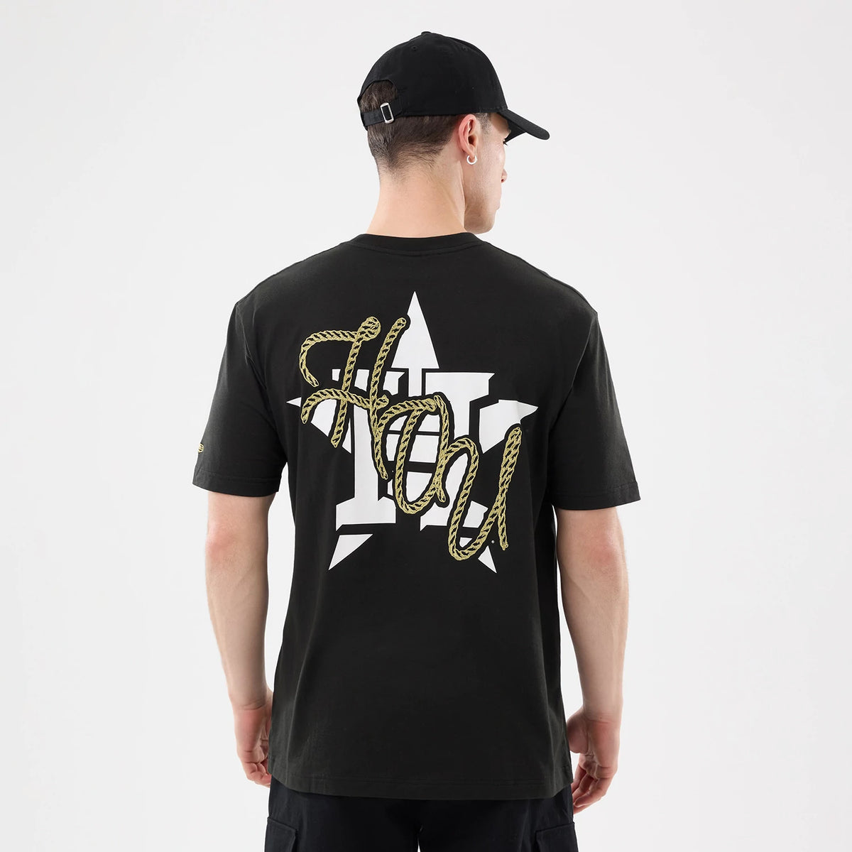 New Era Houston Astros MLB Cowboy Graphic Black T-Shirt, back view on a model with a black cap showing a large white star and rope-style lettering that reads HOU across the upper back, with the New Era logo embroidered on the sleeve.