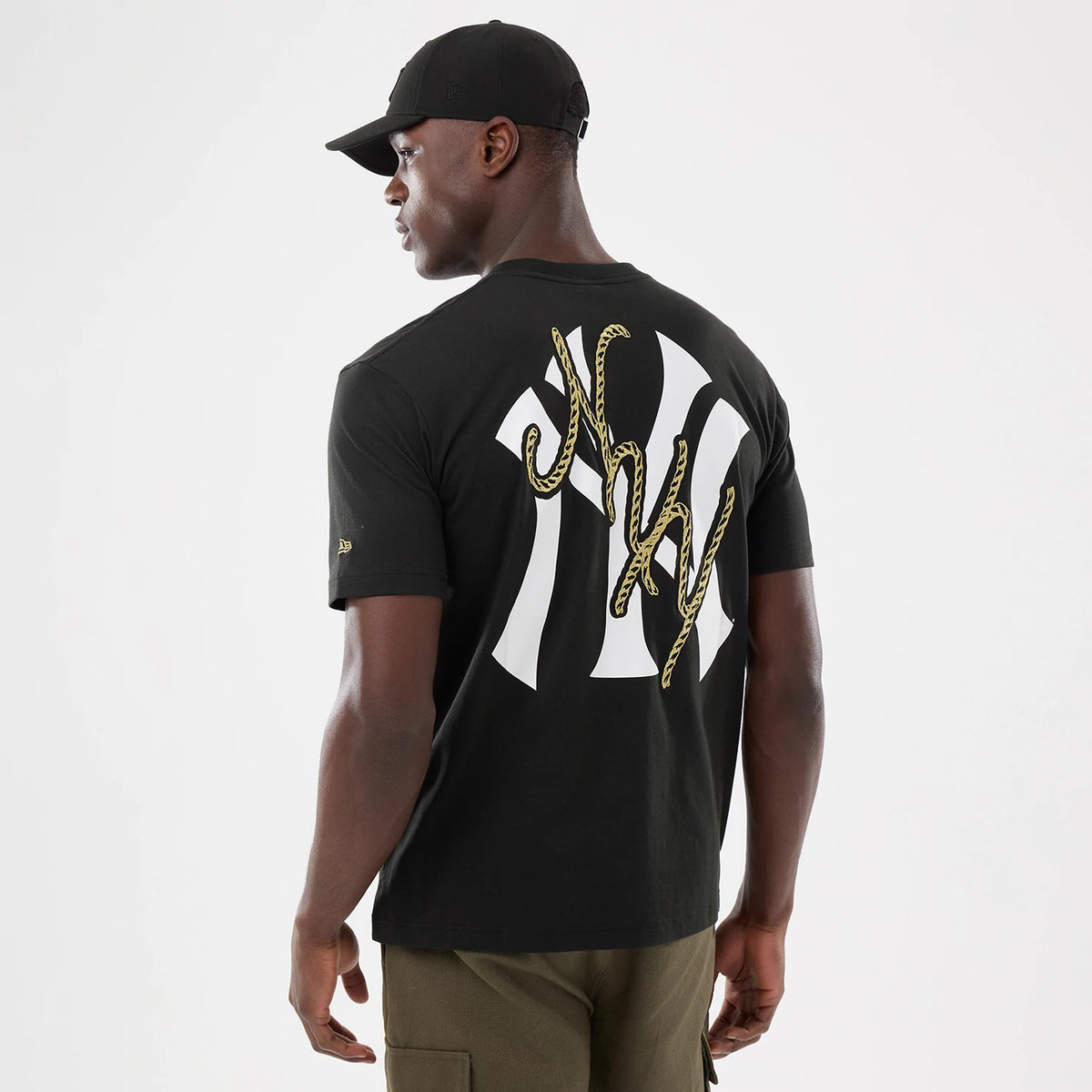 New Era New York Yankees MLB Cowboy Graphic Black T-Shirt, back view on a model wearing a black cap, showing large white Yankees lettering with an overlaid rope design in gold across the back, and an embroidered New Era logo on the sleeve.