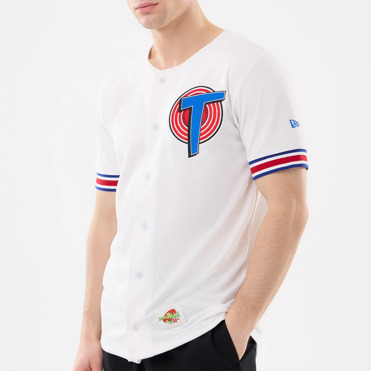 New Era Space Jam Warner Brothers Space Jam White Mesh Jersey, three-quarter view on a model showing a large embroidered T logo on the front, red and blue stripe on the sleeves, and a colourful embroidered patch near the hemline.