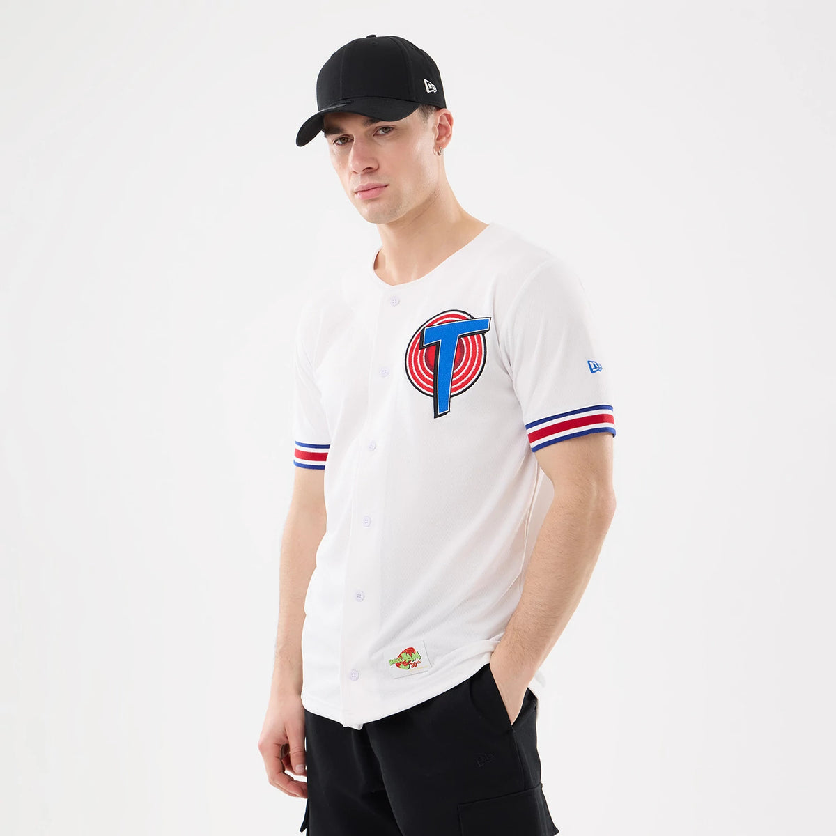 New Era Space Jam Warner Brothers Space Jam White Mesh Jersey, front view on a model wearing a black cap, showing a large embroidered T logo with red and blue accents on the chest and red and blue striped sleeves.