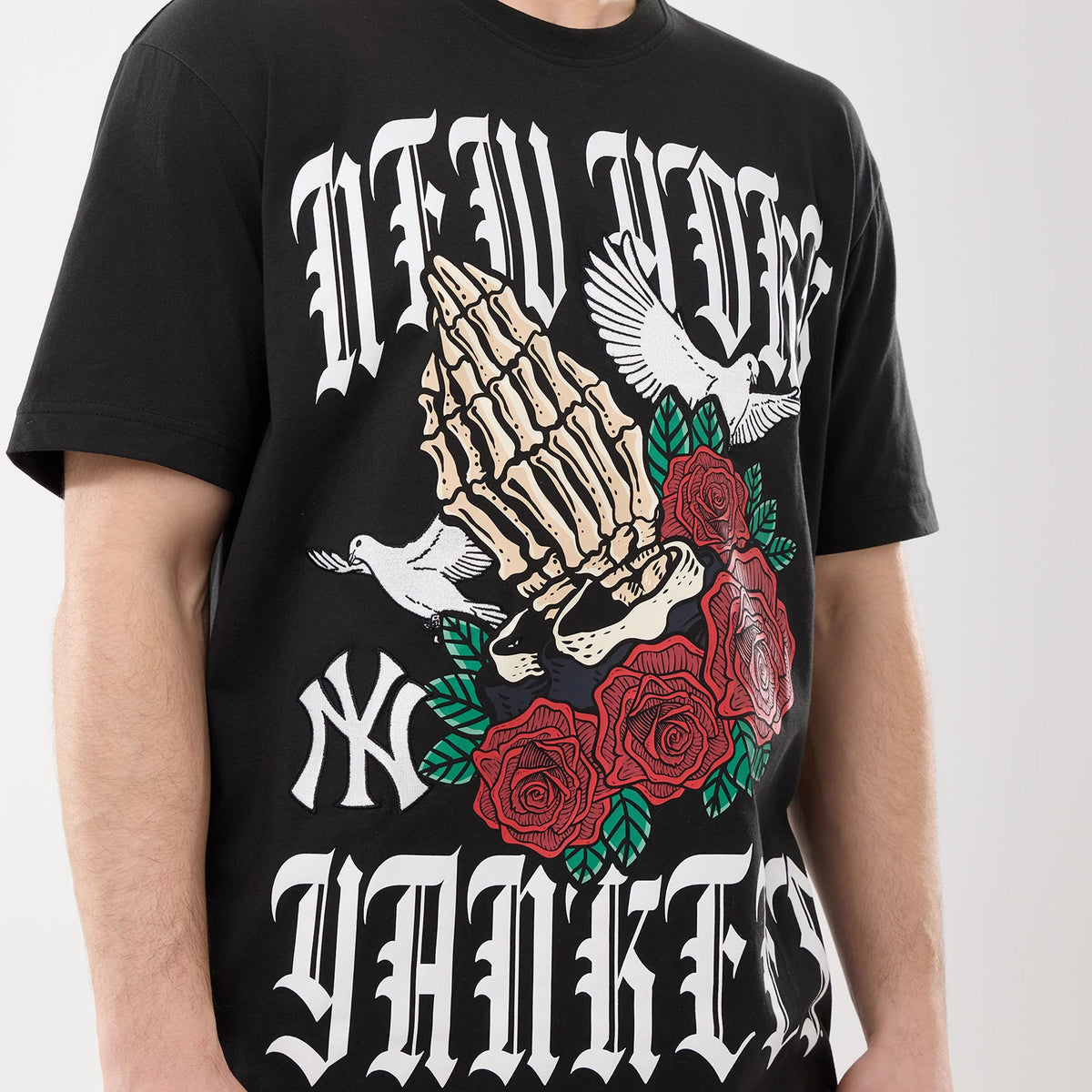 New Era New York Yankees MLB Script Graphic Black T-Shirt, front view showing a print of skeletal hands with roses and doves, white embroidered New Era logo on the lower left, worn by a model.