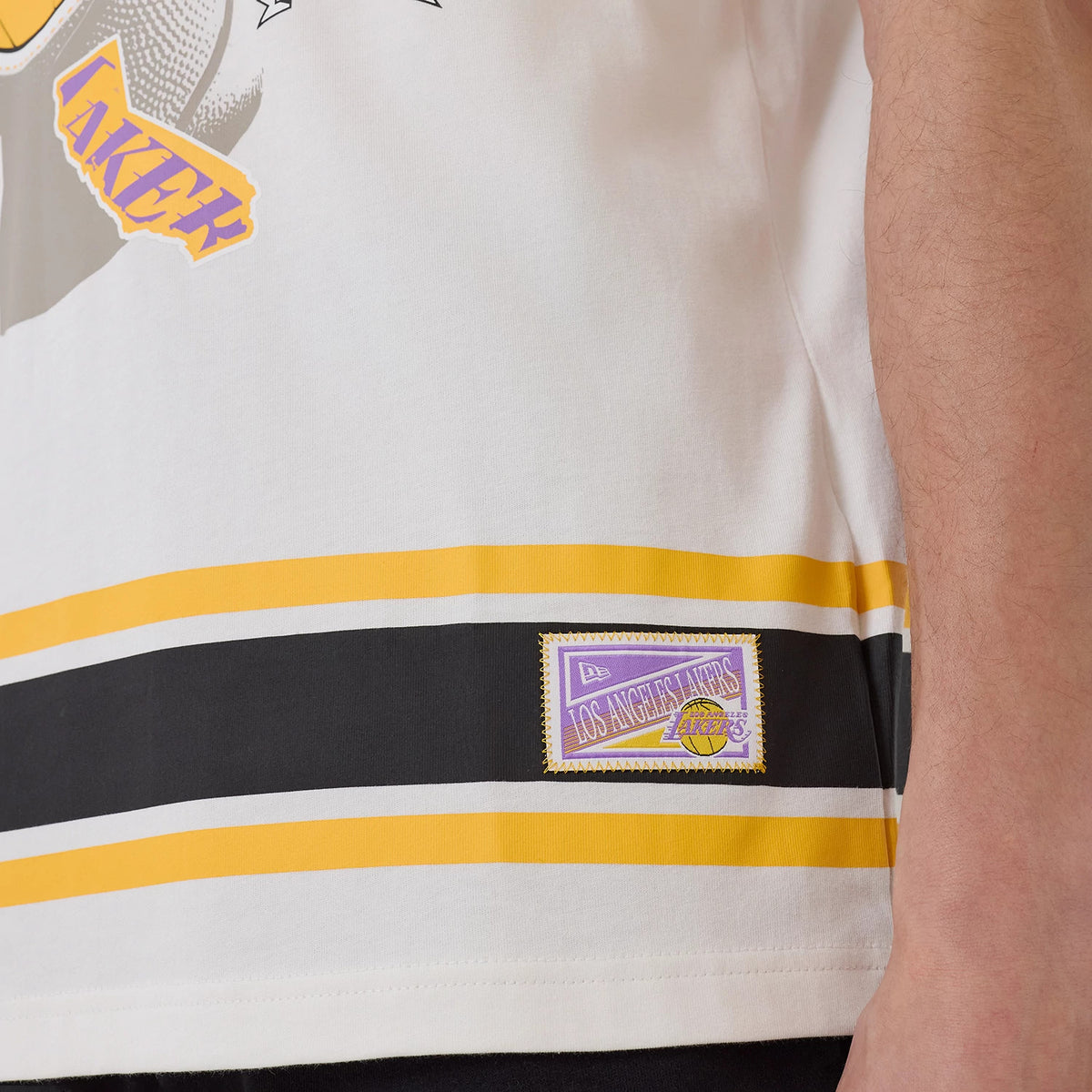 New Era LA Lakers NBA Sport Classic White T-Shirt, side view showing a yellow and black striped hem with an embroidered Los Angeles Lakers badge above it and part of a Lakers graphic just on the upper section.