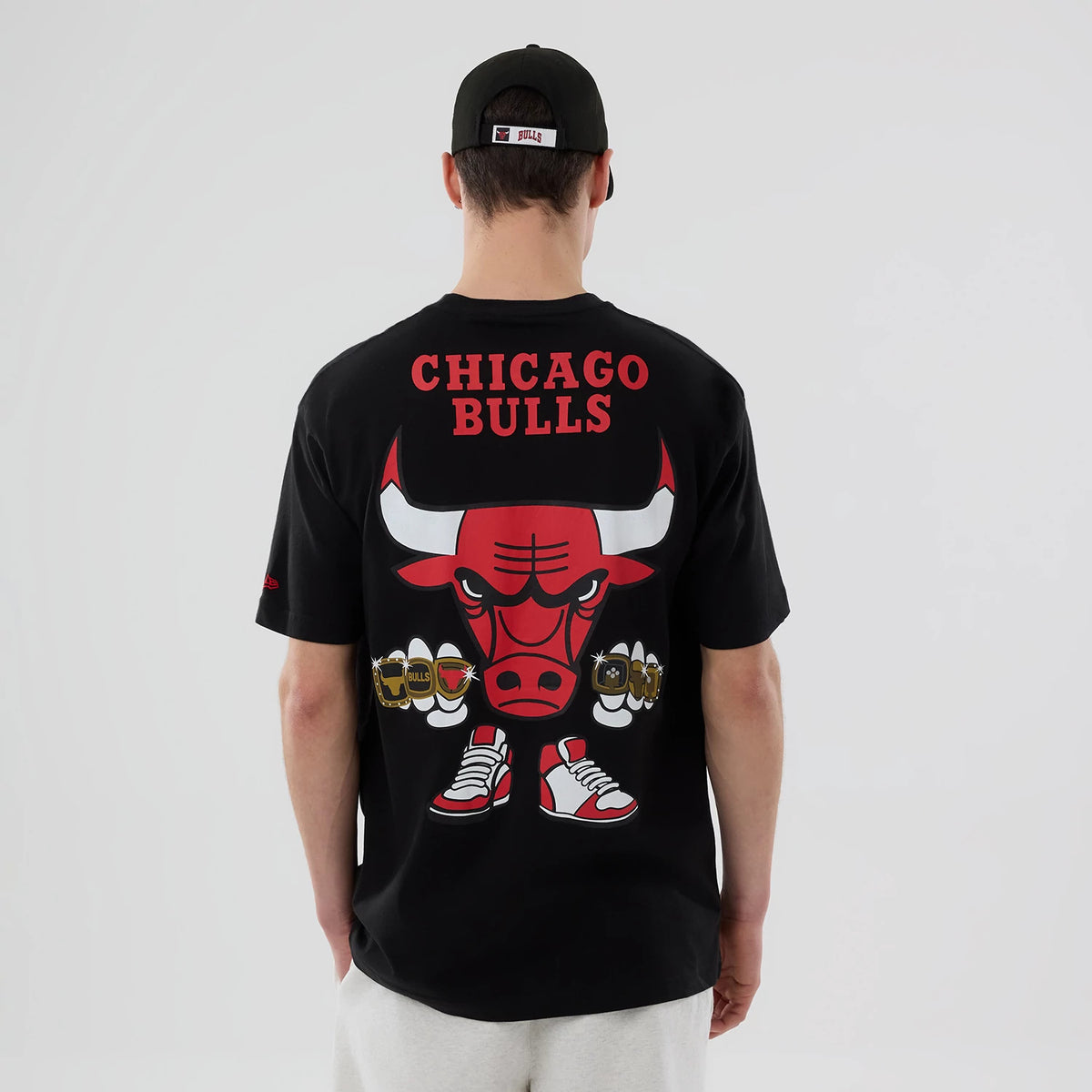 New Era Chicago Bulls NBA Logo Graphic Black T-Shirt, back view on a model showing a large red and white bull graphic with ‘Chicago Bulls’ lettering above, matching shoes illustration below, and a small embroidered logo on the sleeve.