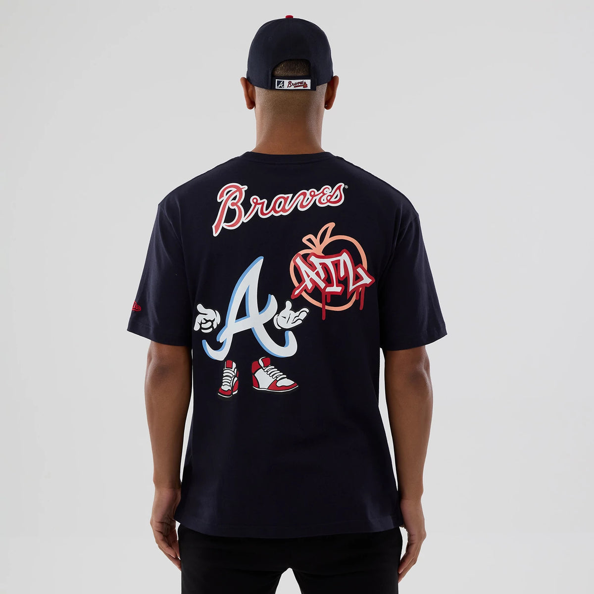 New Era Atlanta Braves MLB Graphic Navy T-Shirt, back view on a model with a navy cap, featuring Braves lettering in white and red at the top, large graphic of the letter A with sneakers and gloves, and ATL graphic to the side.