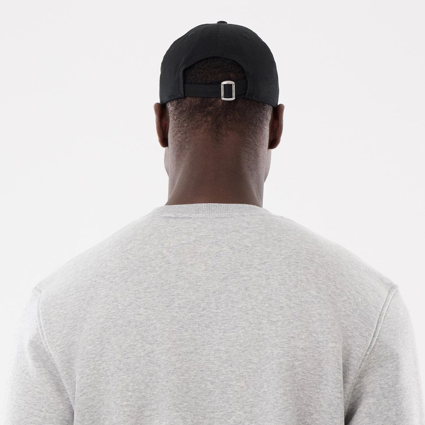 New Era Toronto Blue Jays MLB Sport Classic Grey Crew Neck Sweater, back view on a model showing the light grey fabric and ribbed neck, with the back of a black cap featuring an adjustable strap and buckle.