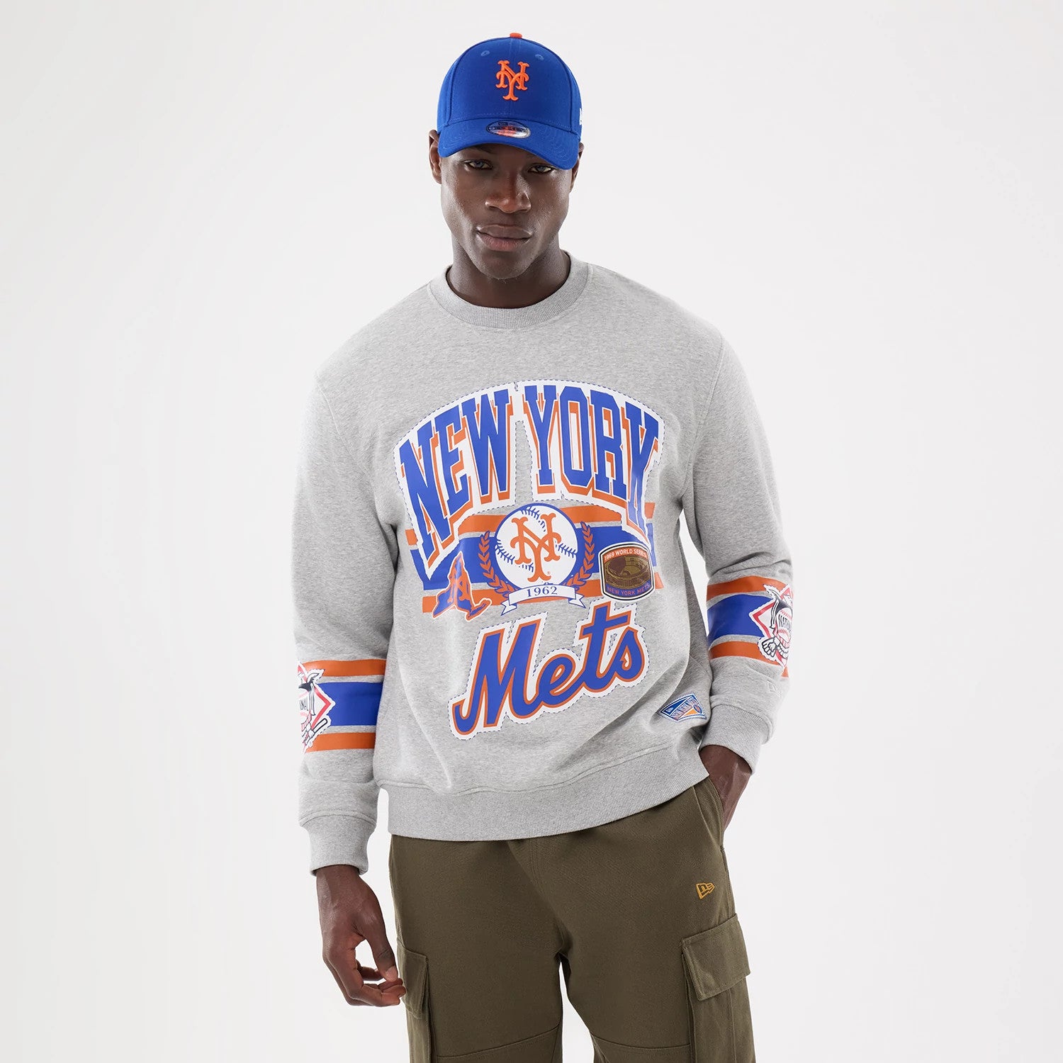 New Era New York Mets MLB Sport Classic Grey Crew Neck Sweater, front view on a model showing large New York Mets graphics across the chest with additional team logos on both sleeves and a ribbed collar and cuffs.