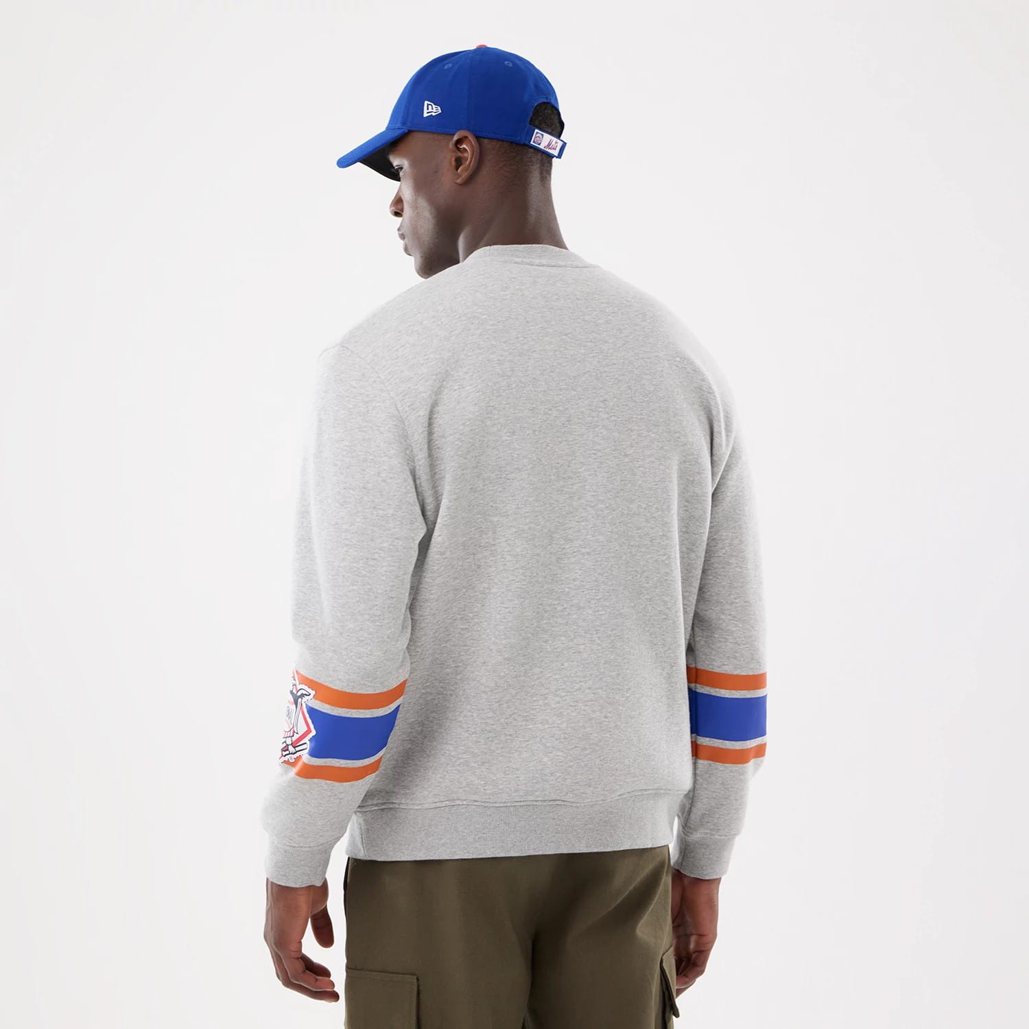 New Era New York Mets MLB Sport Classic Grey Crew Neck Sweater, back view on a model wearing a blue cap, showing a grey knit texture with orange and blue stripes on the sleeves and Mets logo embroidery on the left arm.