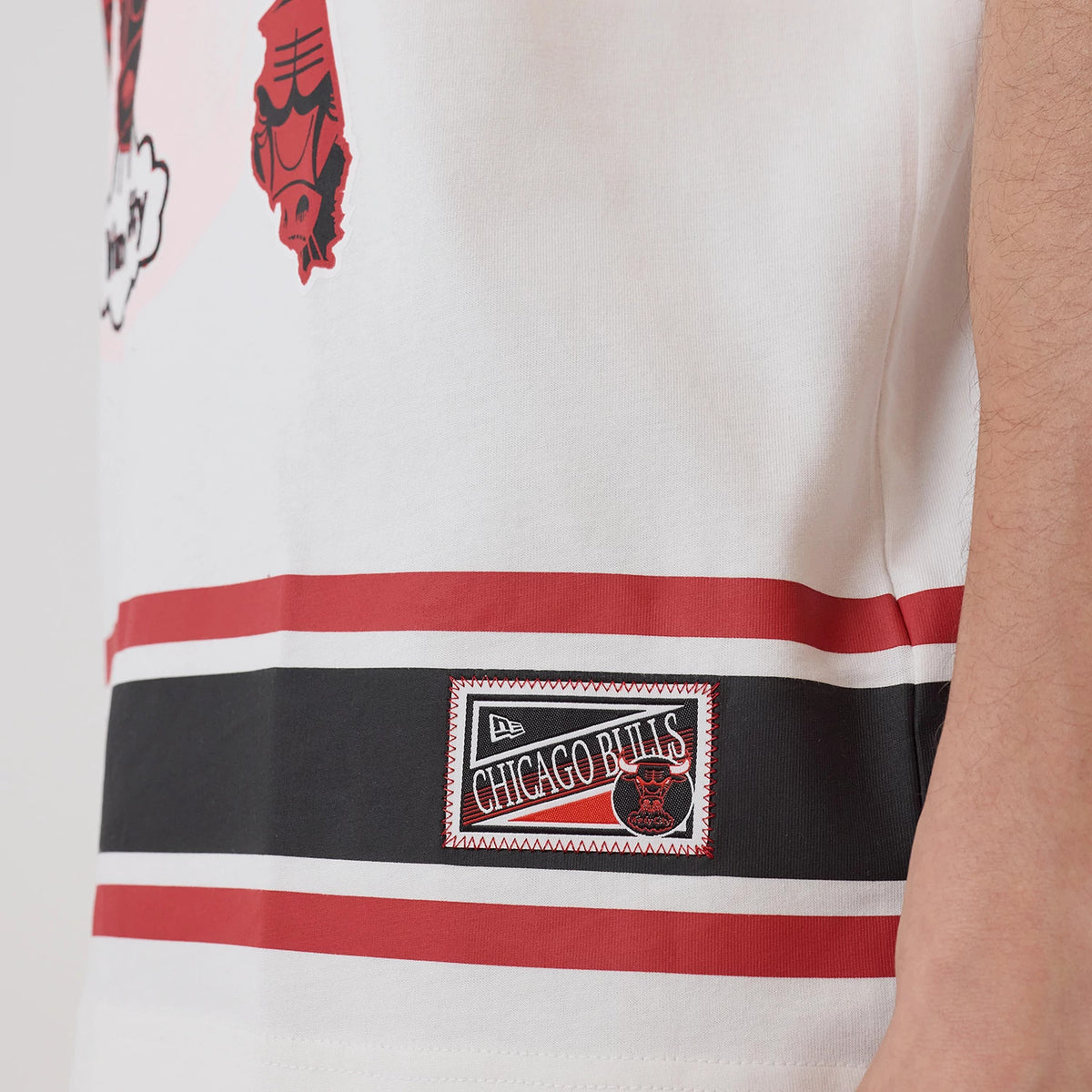 New Era Chicago Bulls NBA Sport Classic White T-Shirt, side view showing a black and red graphic patch with Chicago Bulls text above a bull's head near the bottom hem, with red and black horizontal stripes across the lower section.