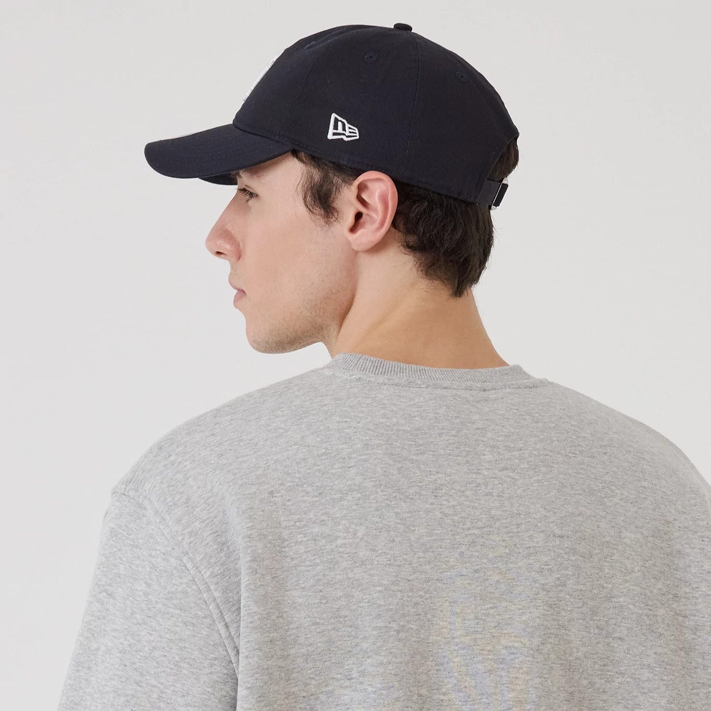 New Era New York Yankees MLB Sport Classic Grey Crew Neck Sweater, on-model rear view showing the grey fabric texture and a relaxed fit, with the wearer also sporting a black cap featuring a white New Era flag logo on the left side.
