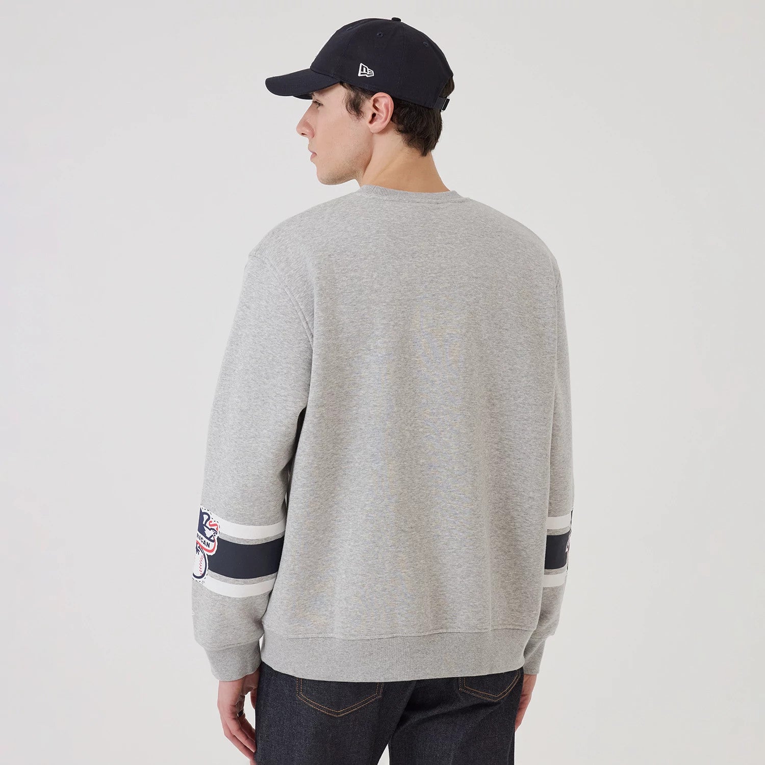 New Era New York Yankees MLB Sport Classic Grey Crew Neck Sweater, back view on a model wearing a matching cap, showing the grey fabric, long sleeves with navy and white stripes, and a relaxed fit.
