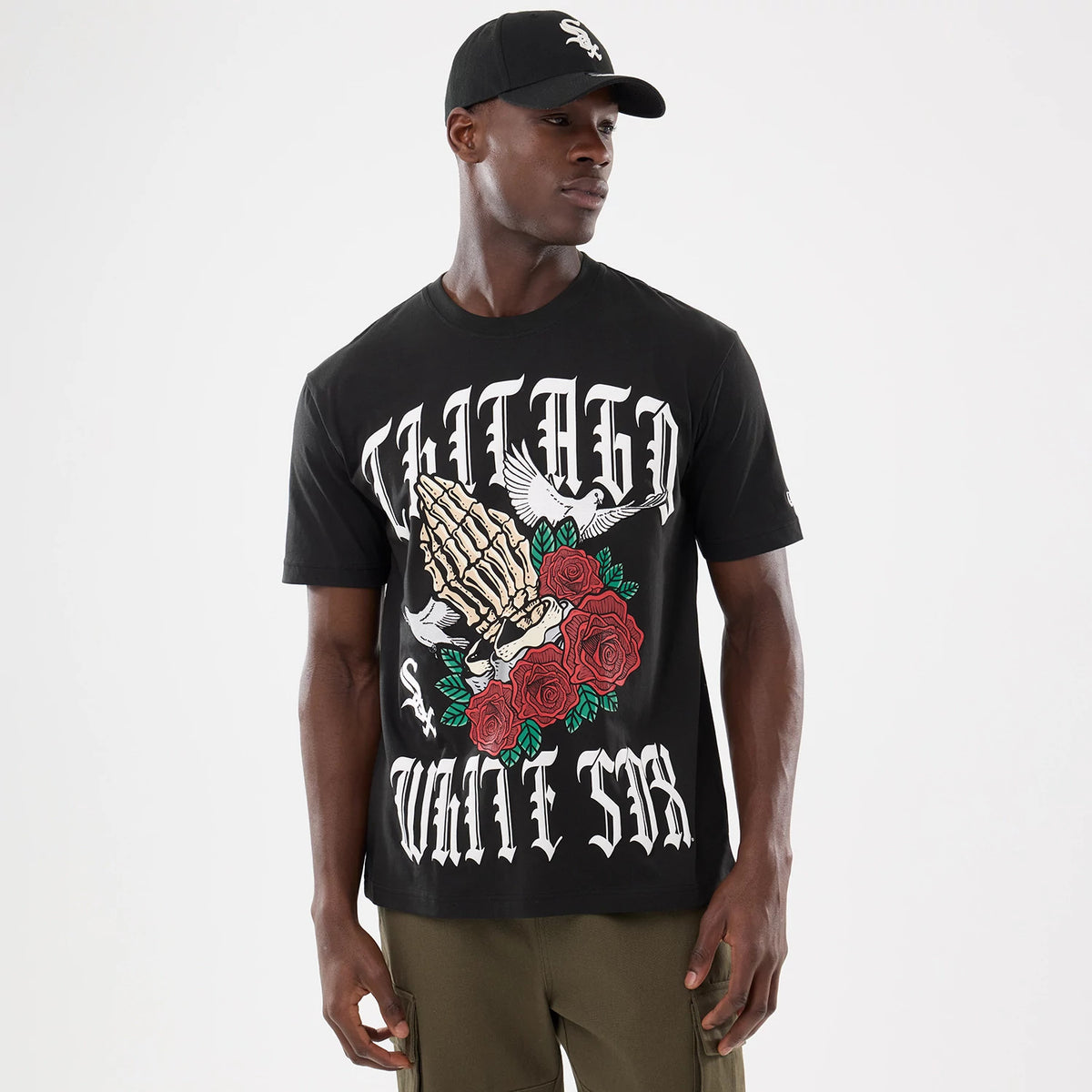 New Era Chicago White Sox MLB Script Graphic Black T-Shirt, front view on-model showing large graphic with skeletal hands, red roses and Chicago White Sox lettering, worn with a matching cap featuring an embroidered team logo.