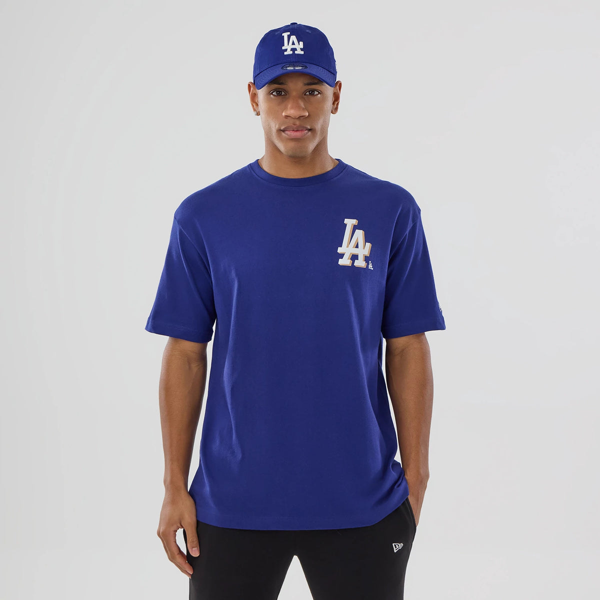 New Era LA Dodgers MLB Graphic Dark Blue T-Shirt, front view on-model showcasing a large LA logo printed on the left chest of the dark blue tee, styled with a matching cap that features an embroidered LA logo at the front.