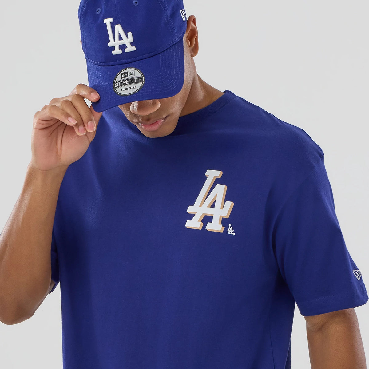 New Era LA Dodgers MLB Graphic Dark Blue T-Shirt, front view on-model highlighting a large white embroidered LA logo on the left chest and styled with a matching dark blue cap featuring the same embroidered logo.