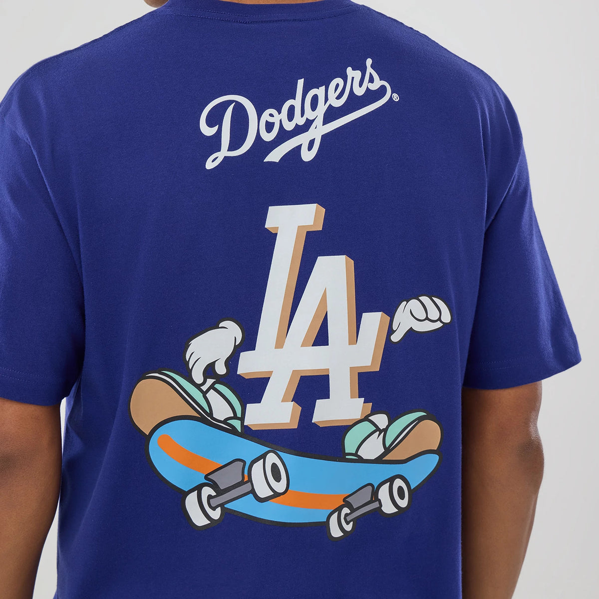 New Era LA Dodgers MLB Graphic Dark Blue T-Shirt, back view on a model showing a large LA graphic with playful gloved hands riding a skateboard and Dodgers script text in white across the upper back.