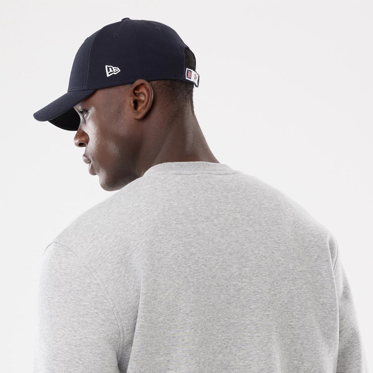 New Era Detroit Tigers MLB Sport Classic Grey Crew Neck Sweater, rear view on a model wearing a dark cap, showing the plain grey fabric and relaxed fit with a neat round neckline, without any logos or embellishments.