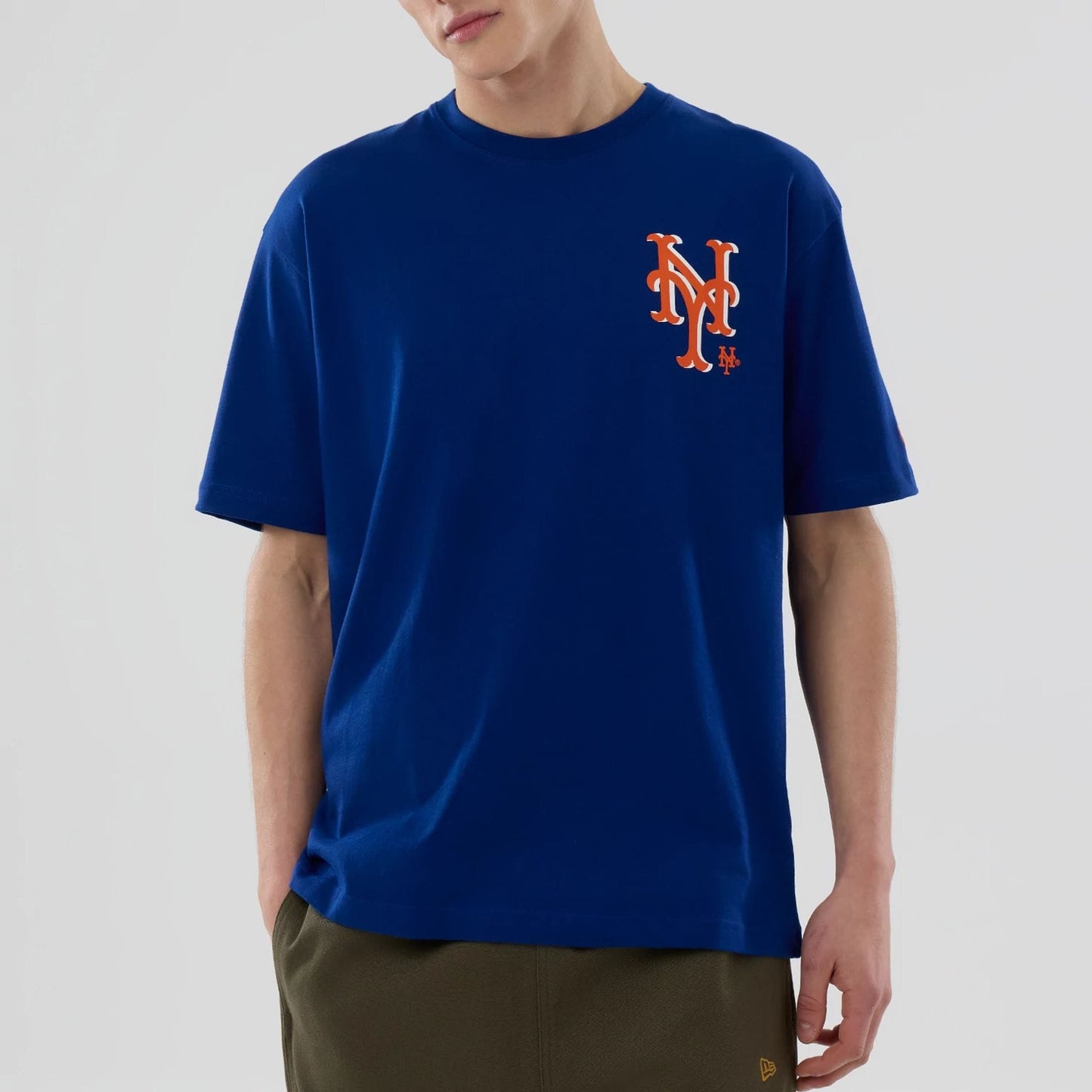New Era New York Mets MLB Graphic Blue T-Shirt, front view displaying the large embroidered orange and white NY logo on the left chest of the blue shirt, worn casually with the sleeves falling naturally on the arms.