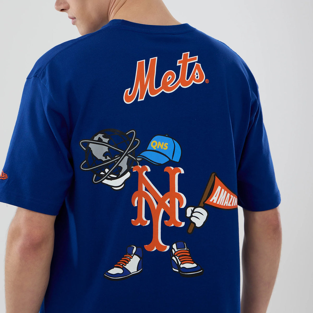 New Era New York Mets MLB Graphic Blue T-Shirt, back view on a model featuring a Mets graphic with a globe, cap, shoes, and the Mets logo, plus Mets text at the neck and a small New Era embroidered logo on the sleeve.