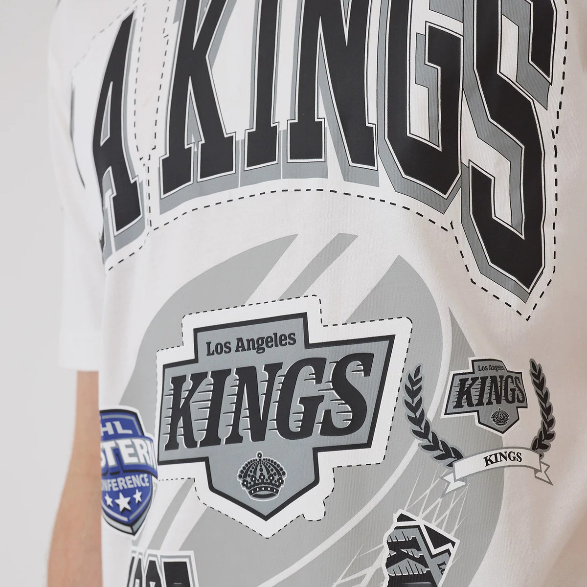 New Era LA Kings NHL Sport Classic White T-Shirt, front view displaying large black and grey LA Kings lettering across the chest with multiple graphic patches and logos, including an embroidered crest reading Los Angeles Kings.