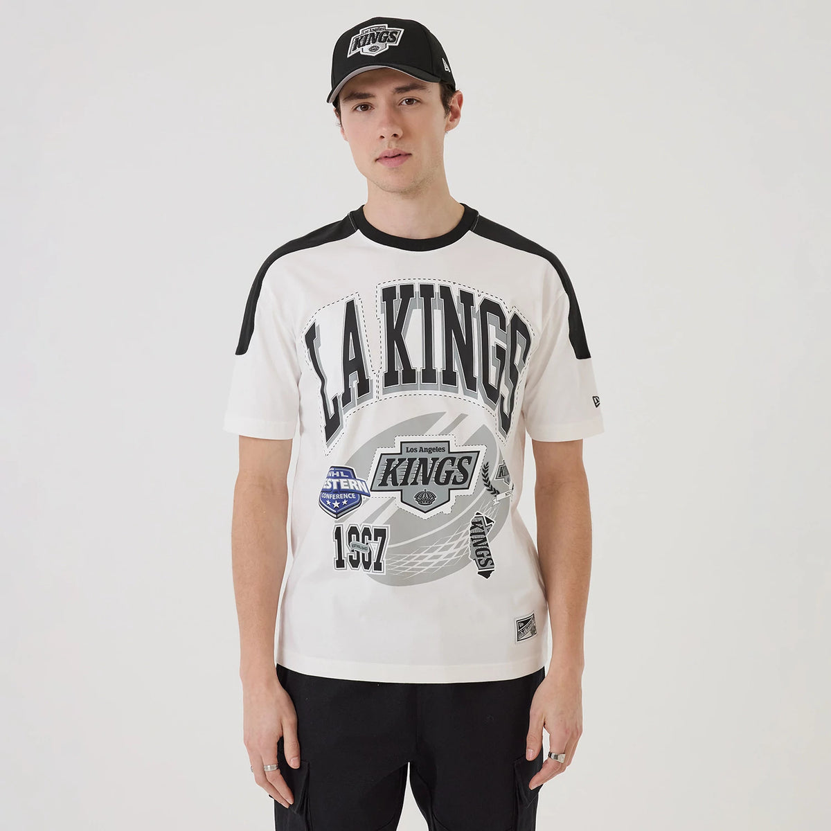 New Era LA Kings NHL Sport Classic White T-Shirt, front view on-model featuring black lettering across the chest, additional graphics including a shield and 1967, with black shoulder details and an embroidered New Era logo on the sleeve.